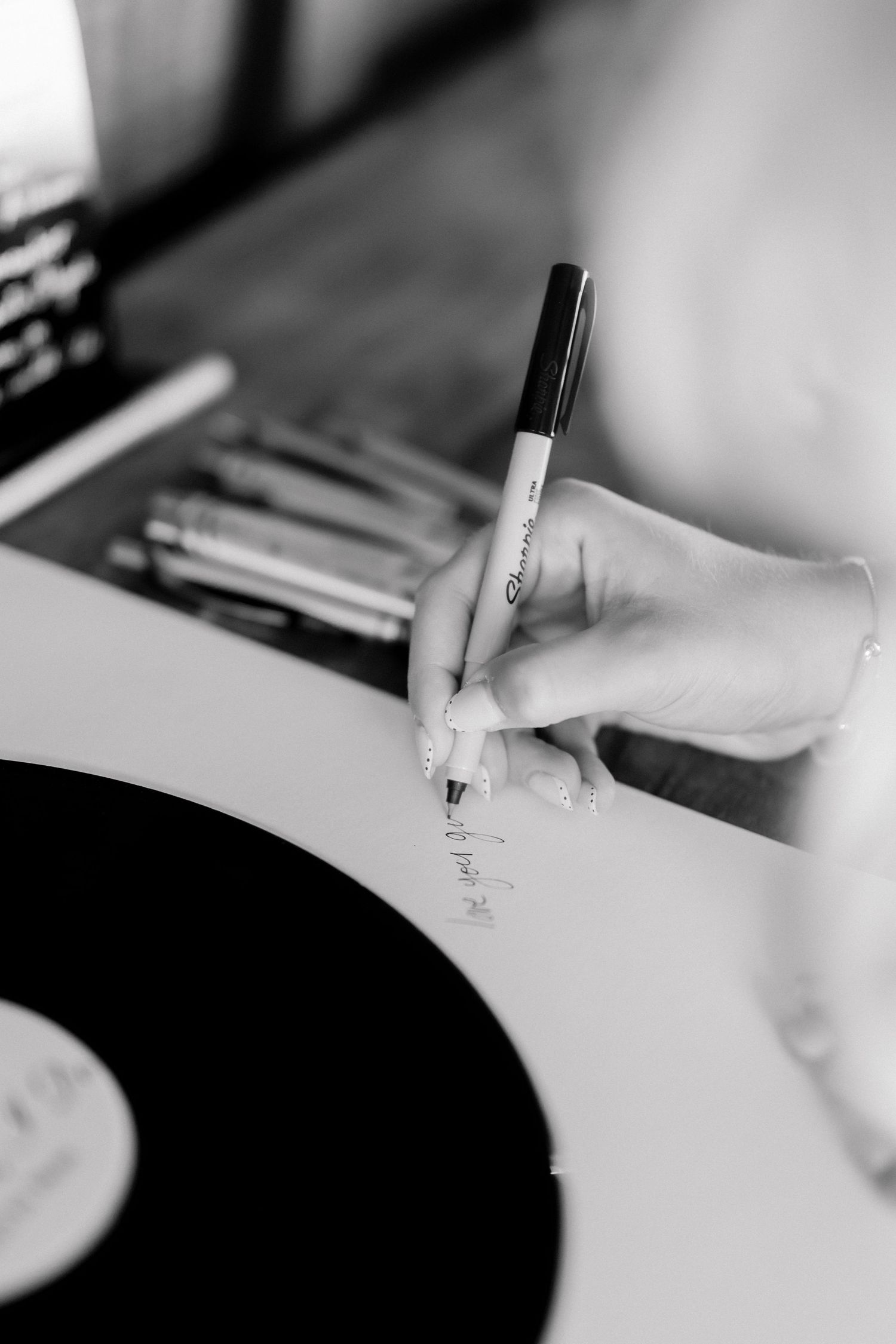 A close-up black and white photo of a hand writing a message with a Sharpie marker on a vinyl record guest book.