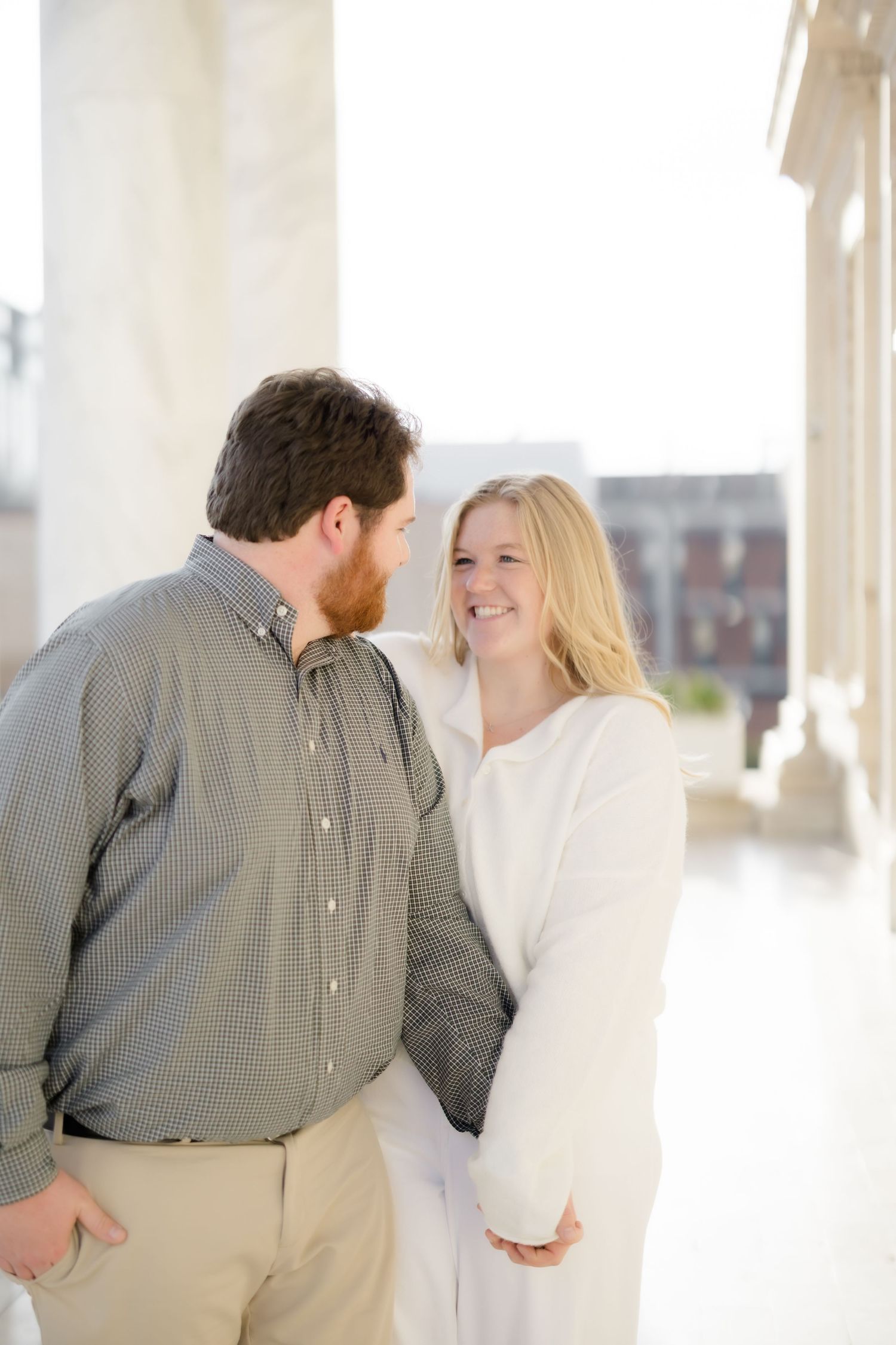 A couple shares a romantic moment, smiling at each other between white columns.