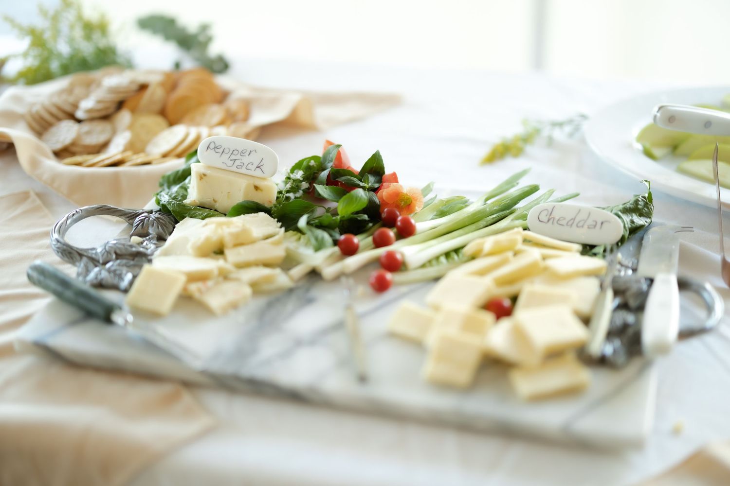 Elegant marble charcuterie board with assorted cheeses, fresh vegetables, crackers, and decorative labels at a catered event.