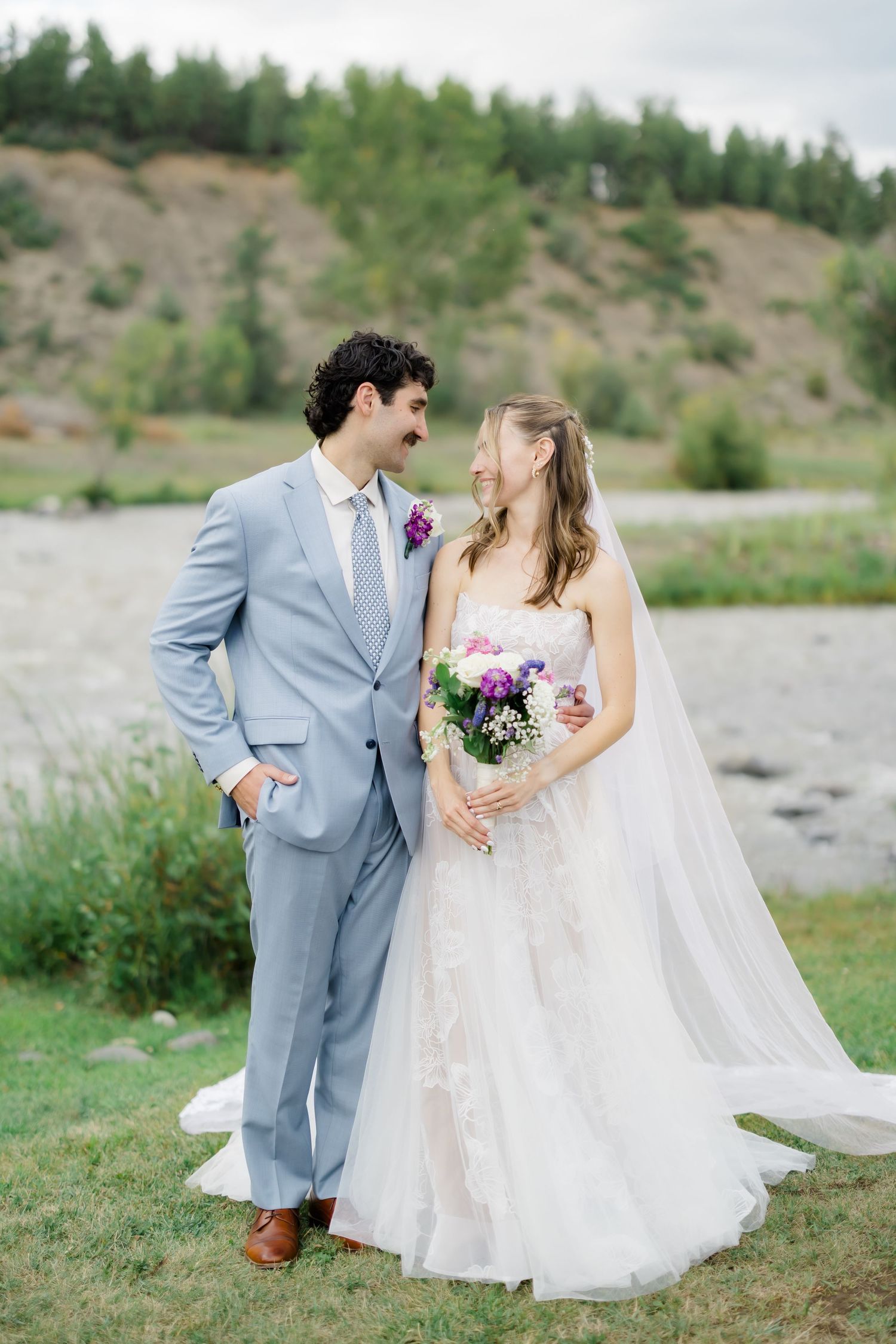 A romantic bride and groom in light blue suit and gown share intimate moments in a scenic outdoor setting in Pagosa Springs, Colorado.