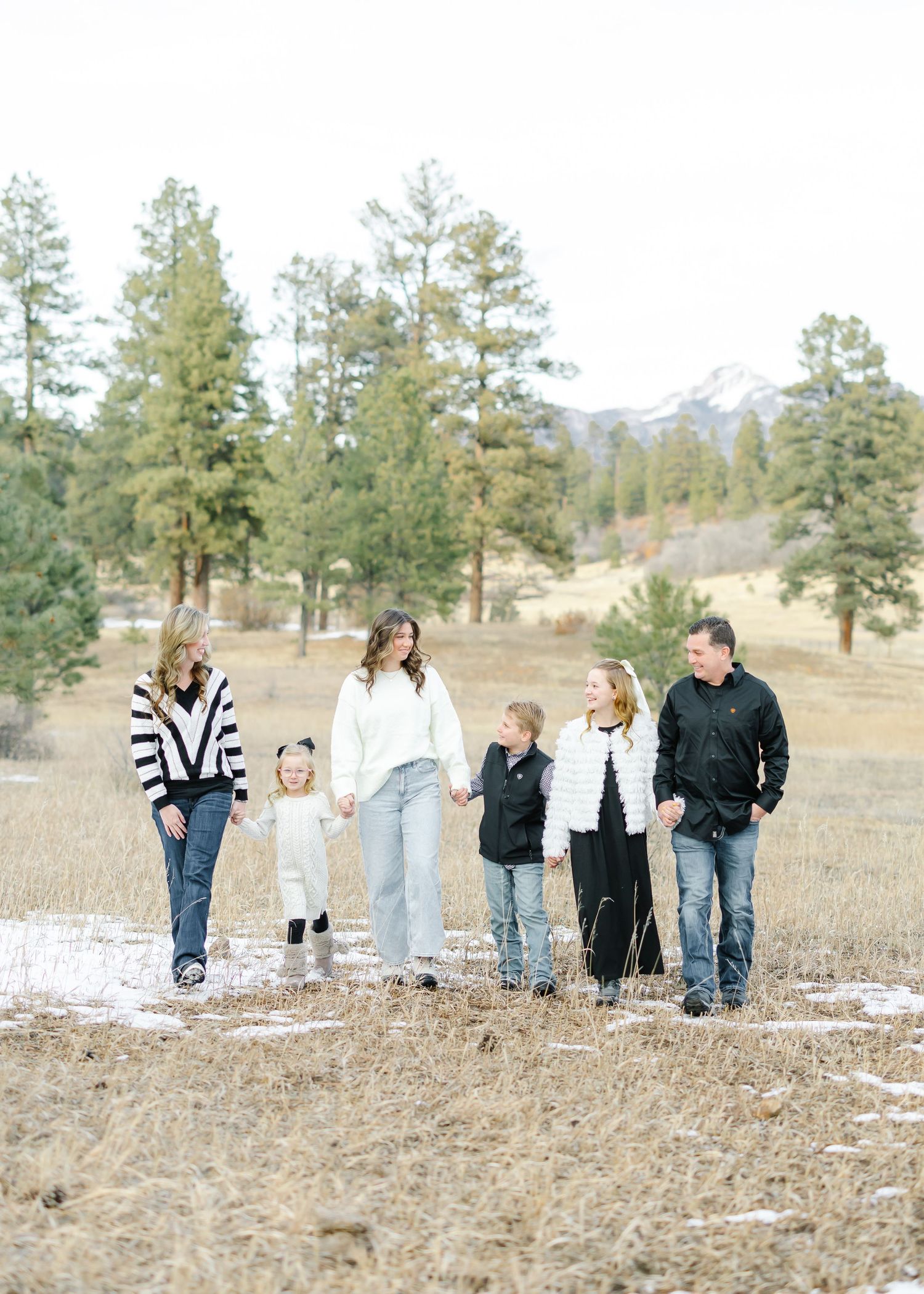 Family group walking together through a grassy field with pine trees and mountains in the background.