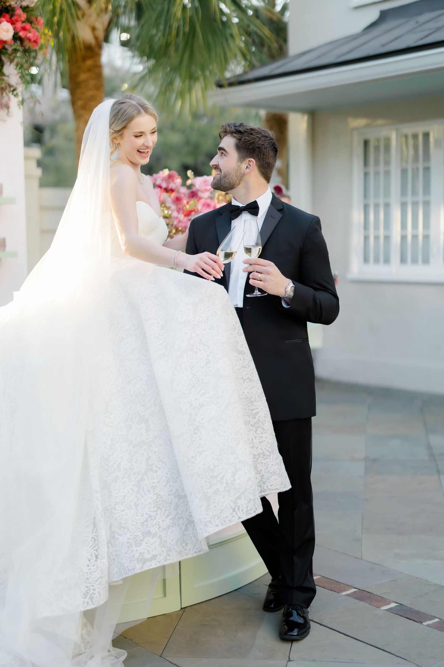A wedding couple shares an intimate moment outdoors near palm trees and a white building.