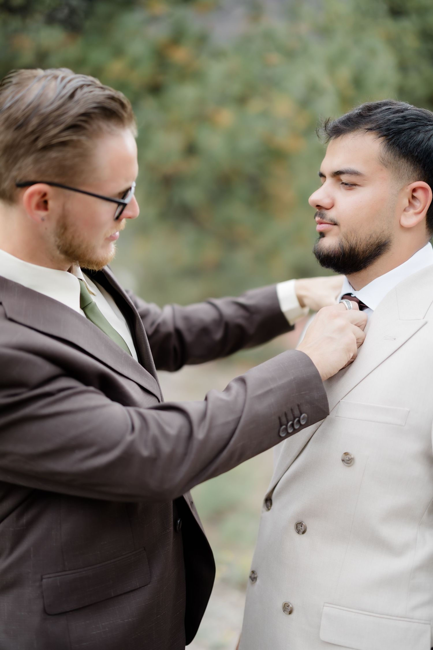 Two men in suits adjusting a tie outdoors, perfect for wedding or formal event styling inspiration.