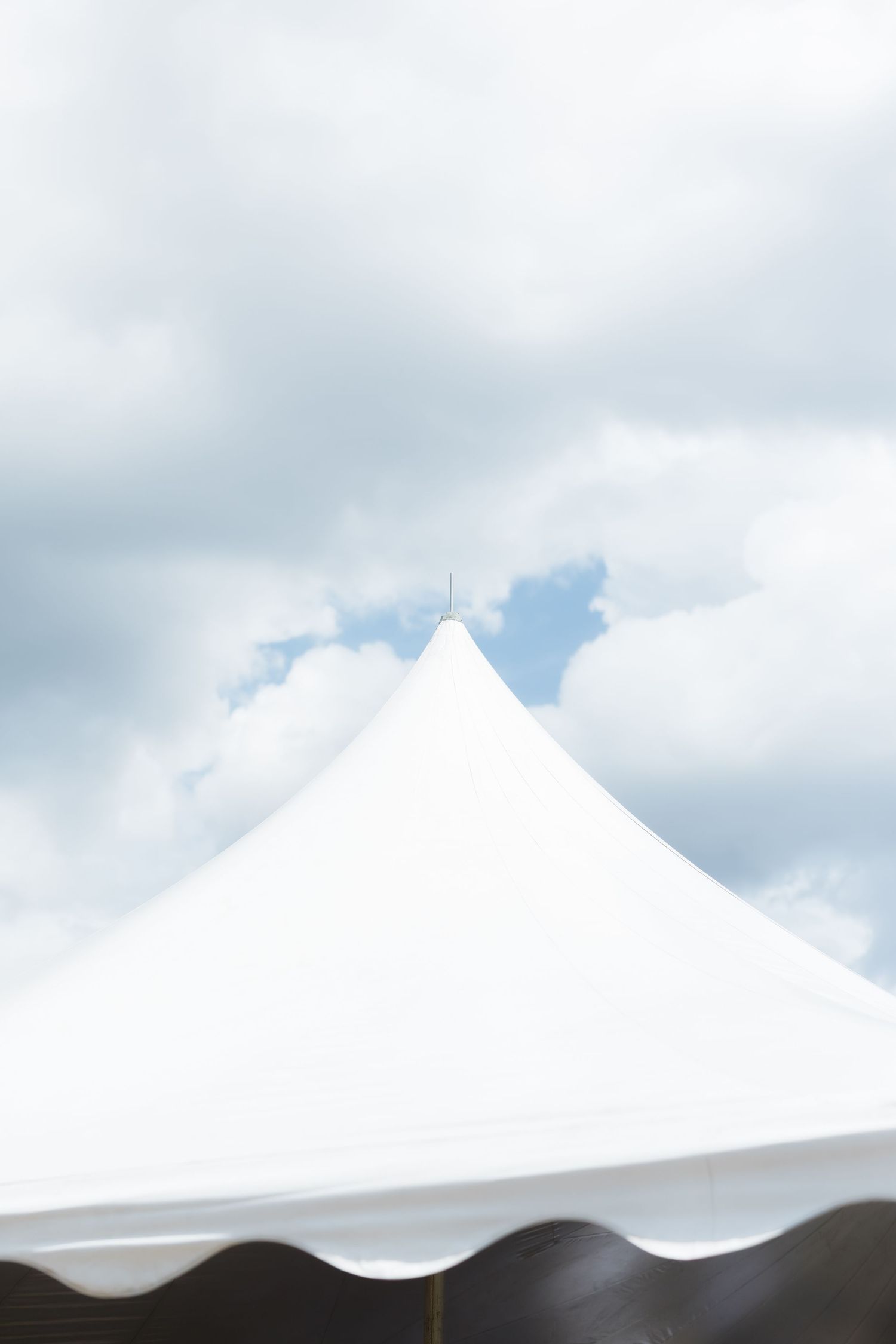 White peaked tent top against a partly cloudy blue sky, ideal for outdoor events and celebrations.