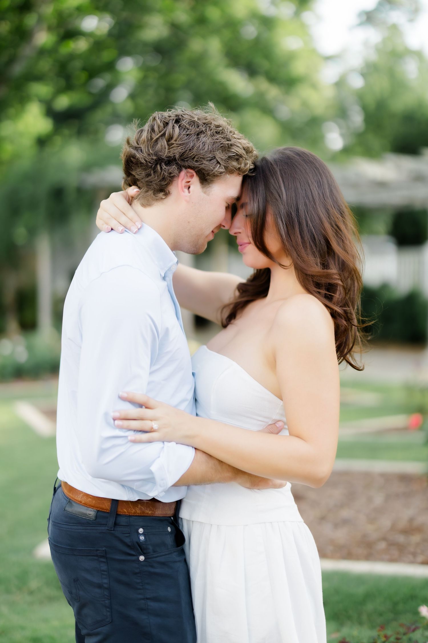 Couple embracing forehead to forehead in a lush garden during an outdoor engagement photo session.