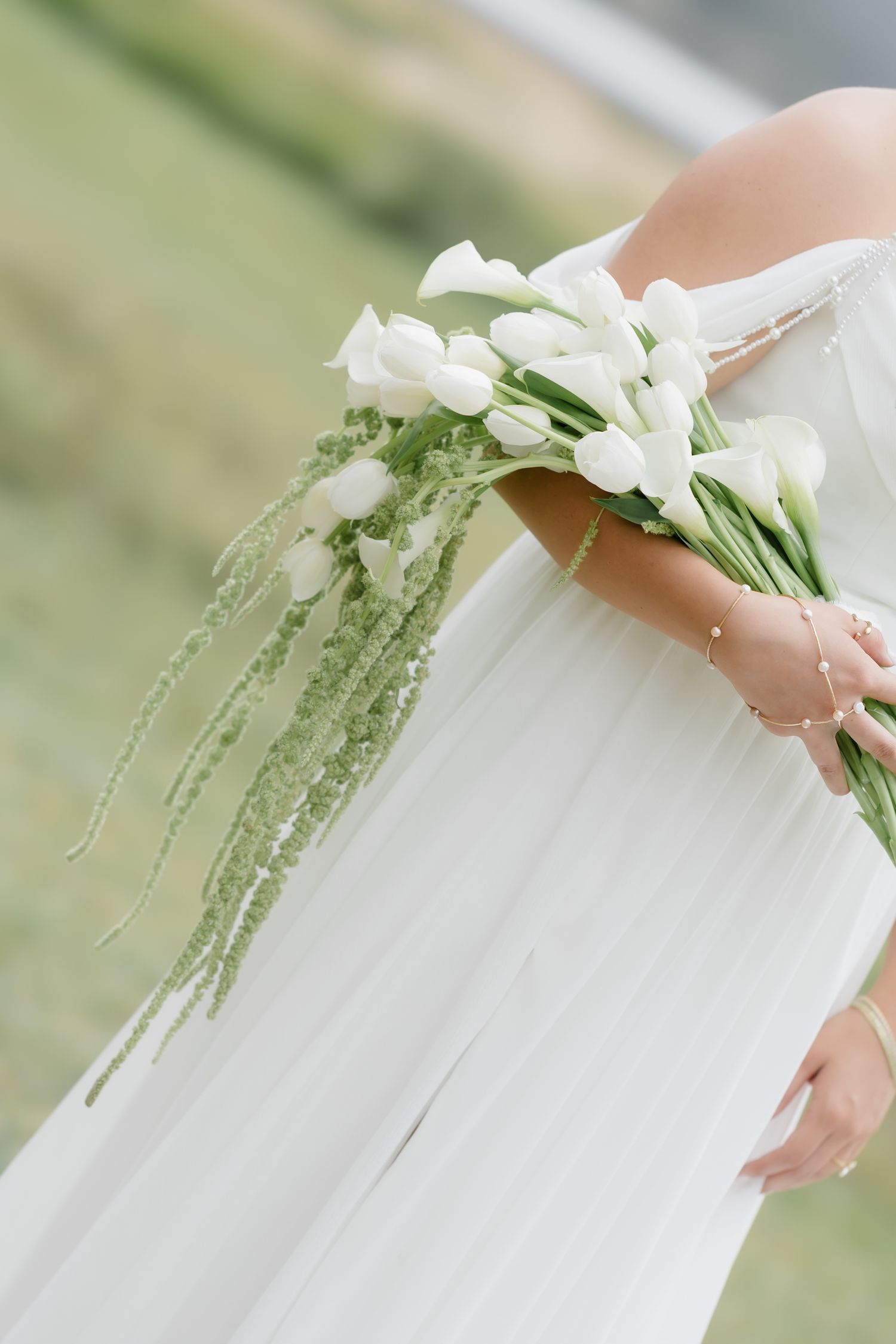 Bride in white gown holding elegant bouquet of white tulips with cascading green amaranthus.
