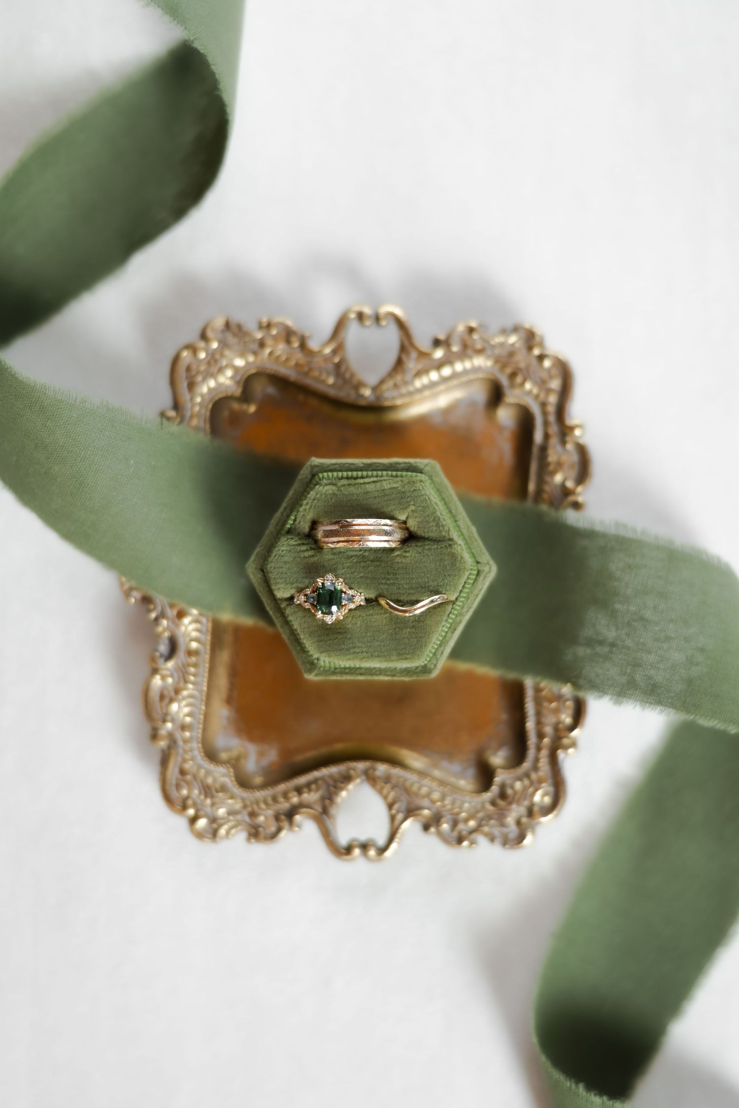 Gold rings with green gemstone in sage velvet hexagon ring box on ornate gold tray with green ribbon.