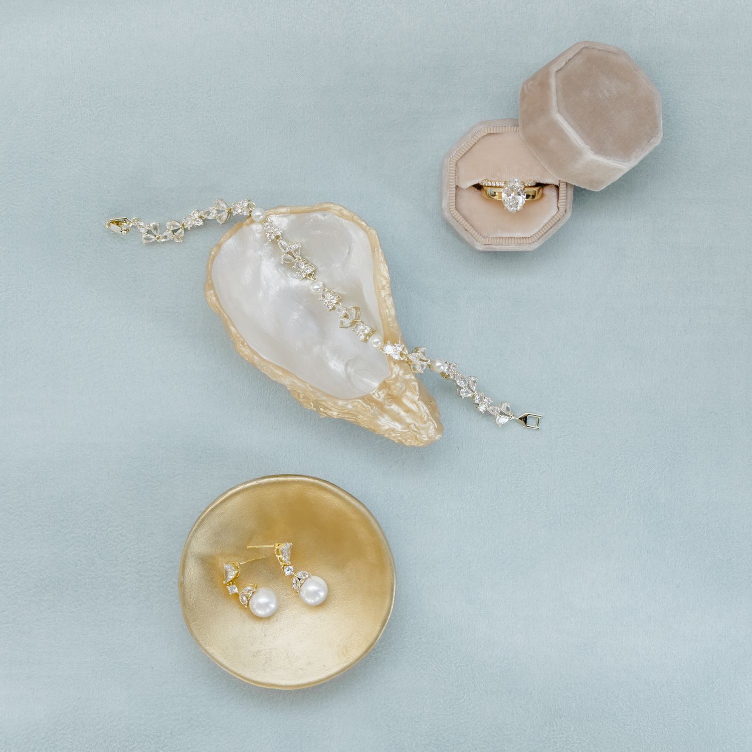 Pearl and diamond jewelry pieces displayed on a soft blue velvet background. Gold and white oyster shell.