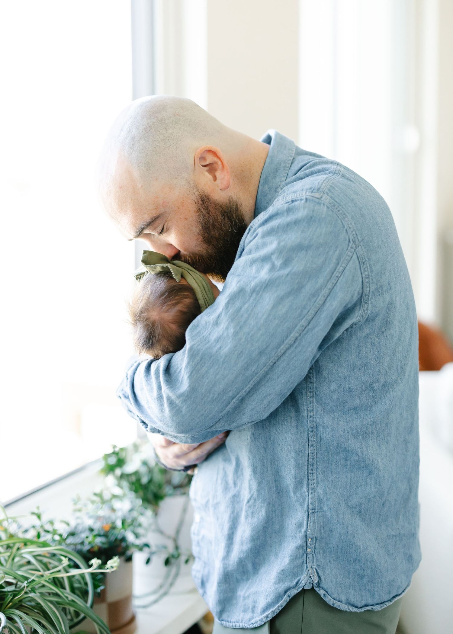 Father in denim shirt holding his newborn and kissing her on the forehead.
