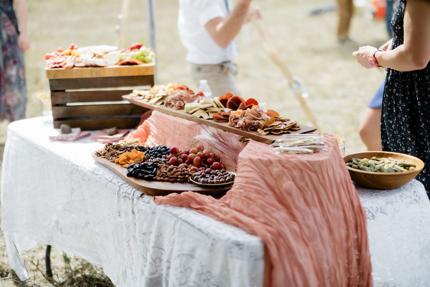 Elegant outdoor grazing table with charcuterie, fruits, and appetizers on a lace tablecloth with a pink runner.