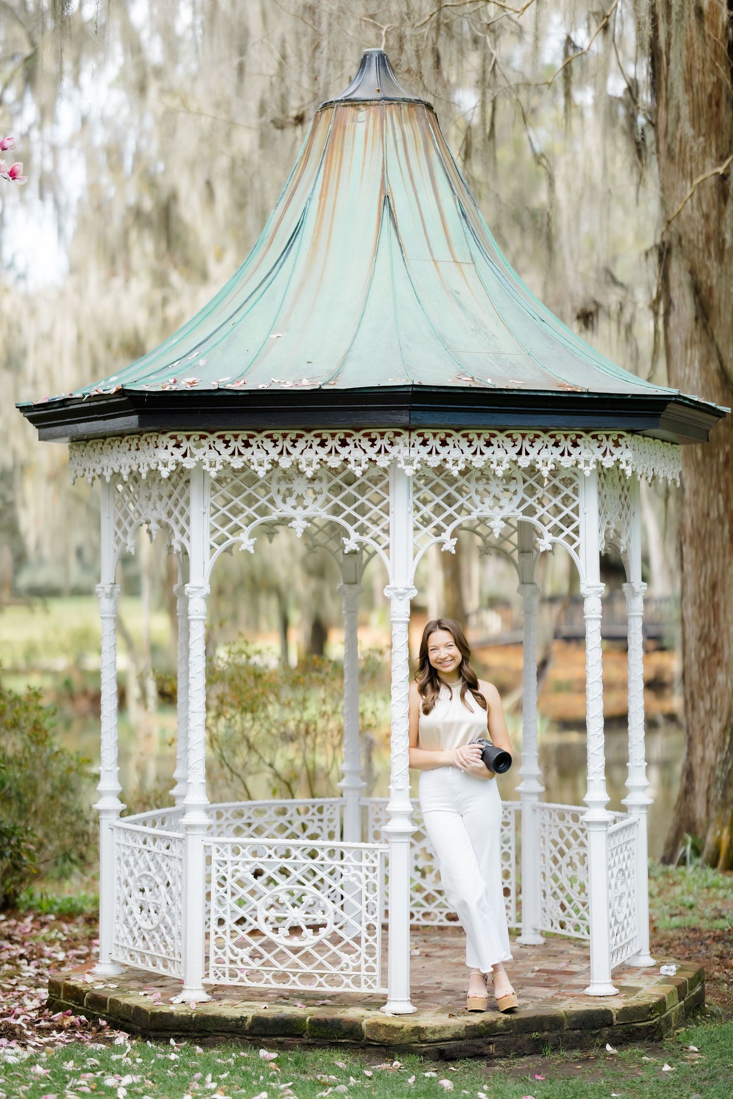 Charming white gazebo with ornate details and mint green roof surrounded by Spanish moss in a garden setting.