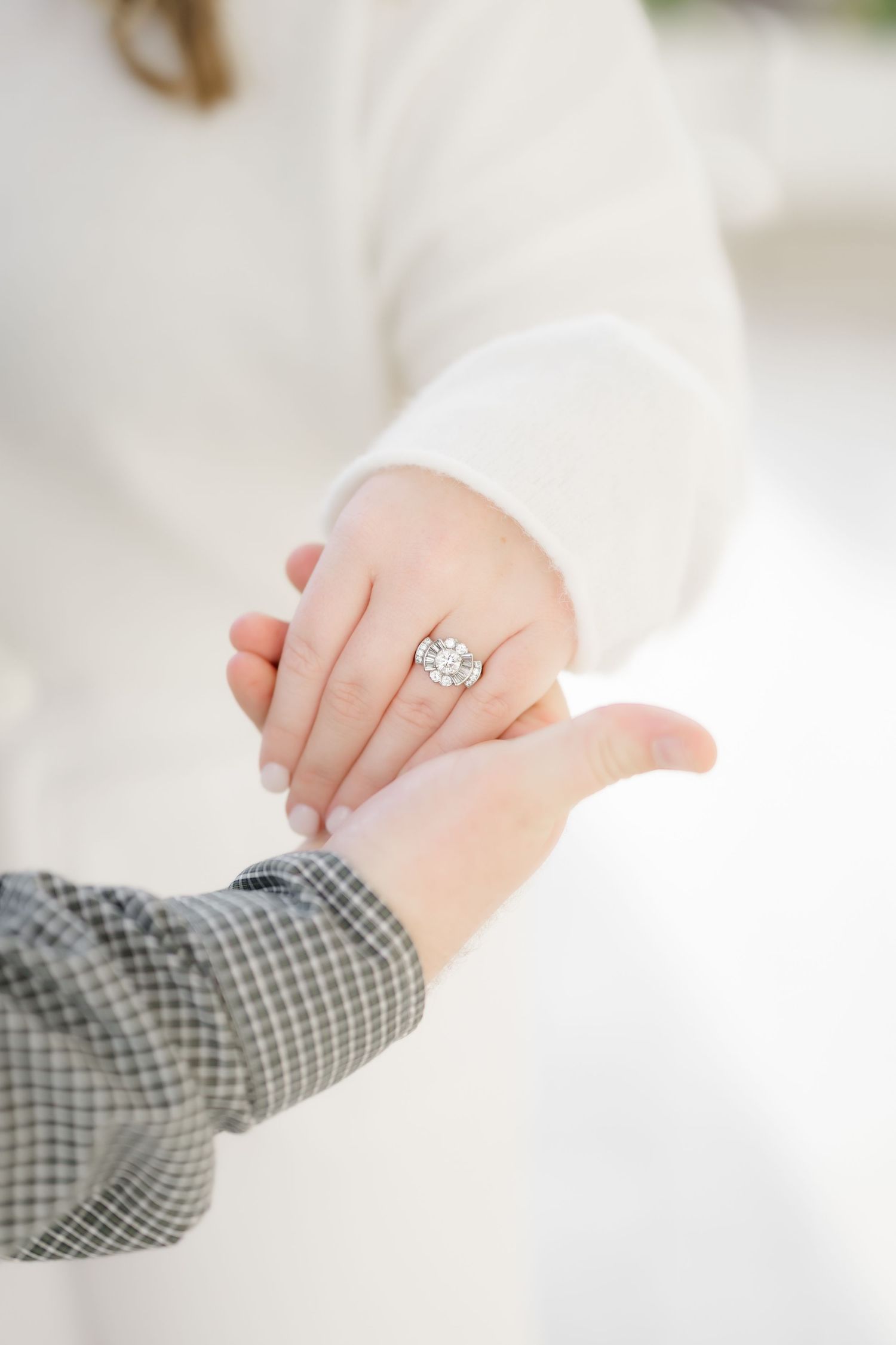 Close up of hands showing an heirloom art deco engagement ring against a white background.