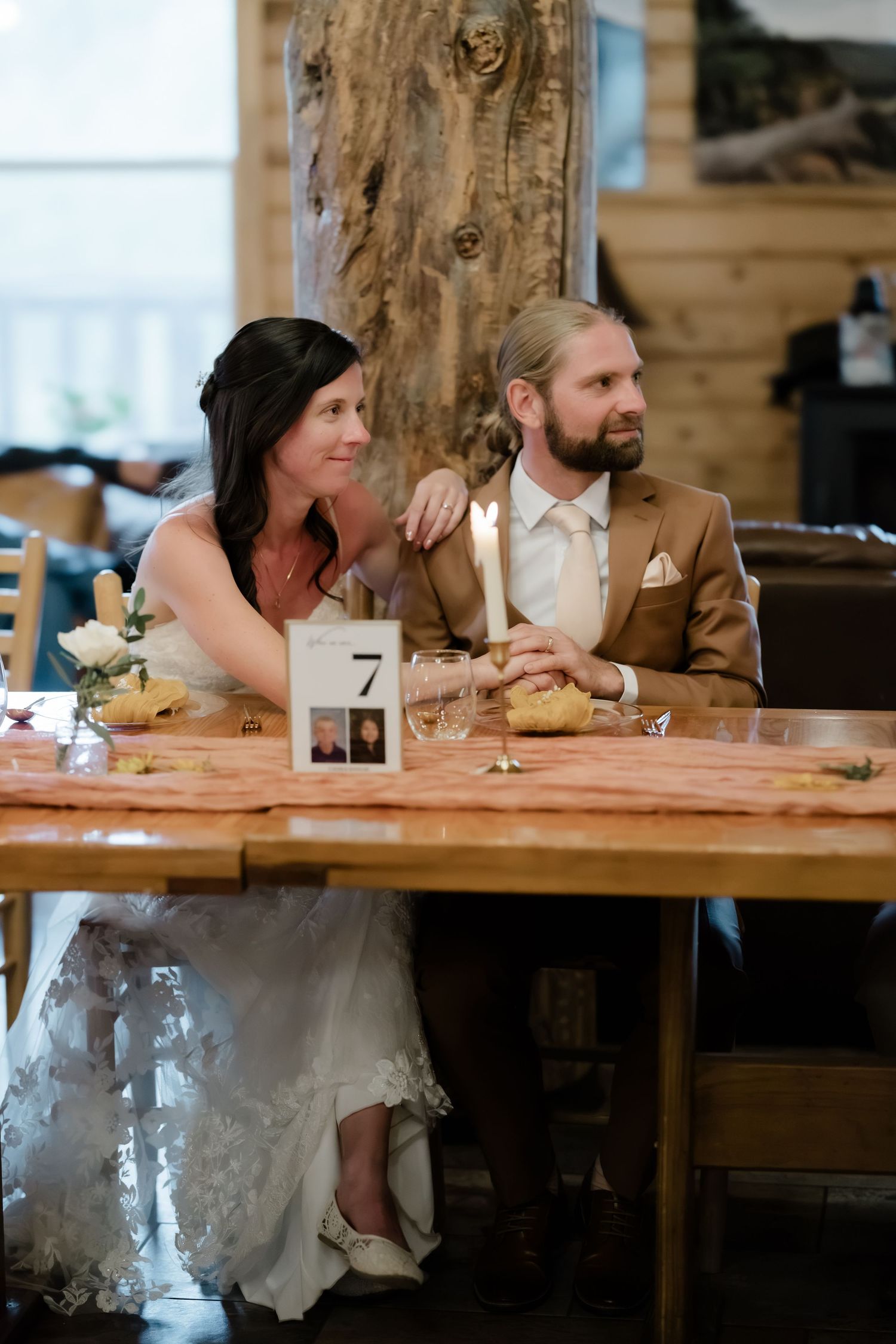 Bride and groom sitting together at a rustic wooden table during their wedding reception in a log cabin venue.