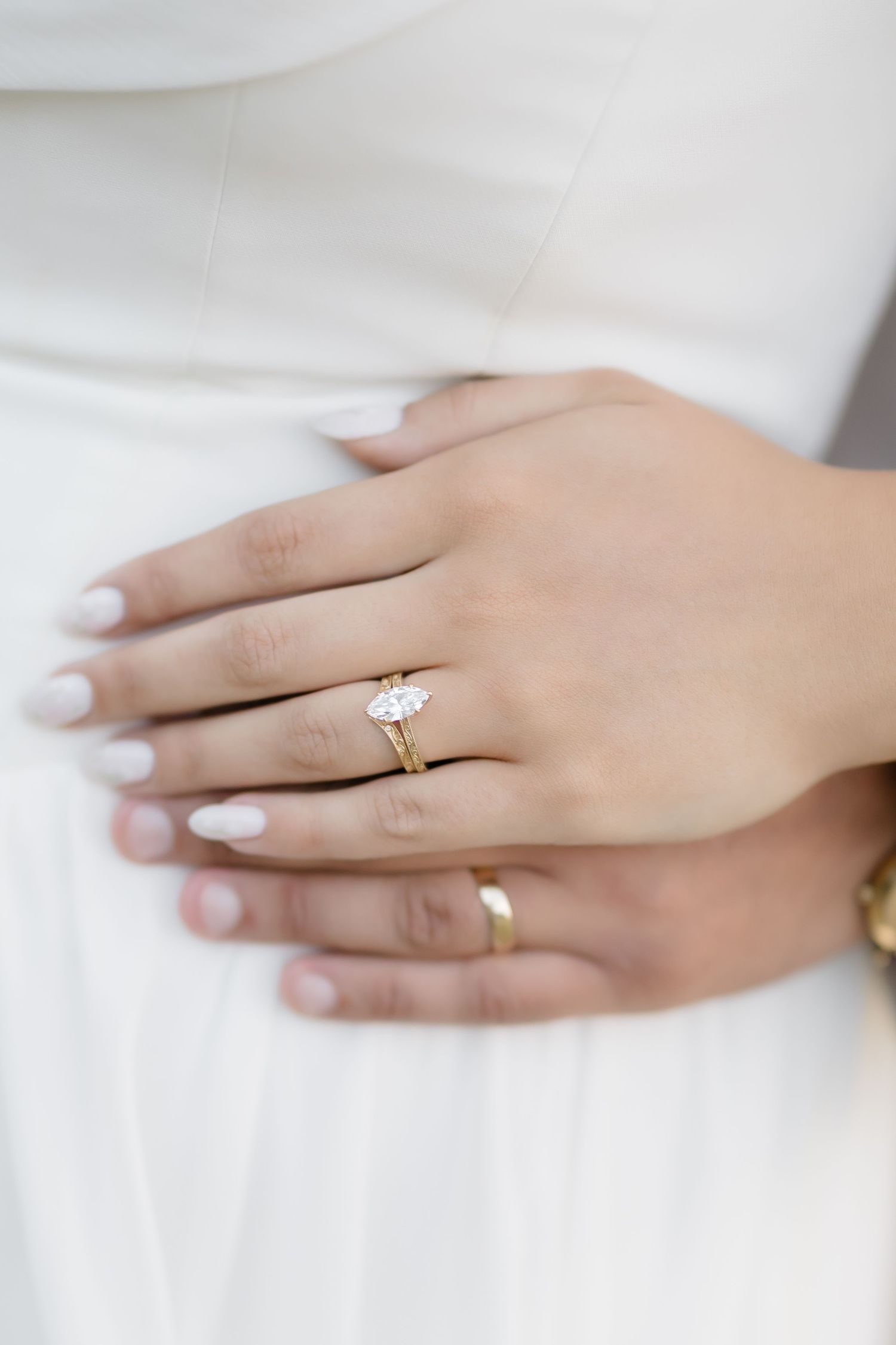 Close-up of a gold engagement ring with marquise diamond on a bride's hand with white manicure.