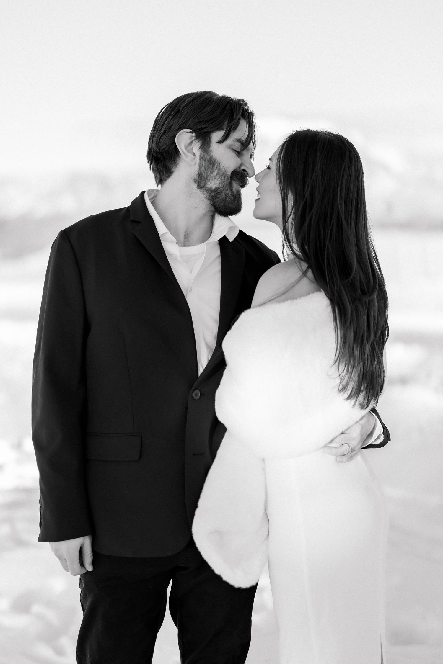 Black and white photo of a bride and groom sharing a romantic kiss in a snowy winter wedding setting.