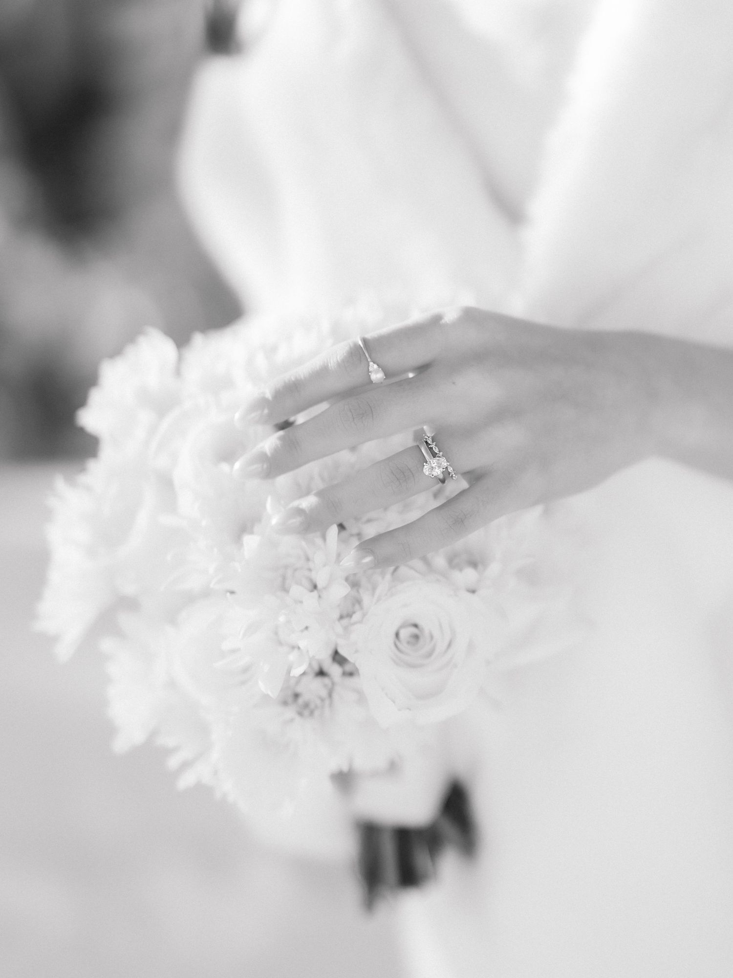 Black and white photo of a bride holding a white floral bouquet, showcasing an elegant diamond engagement ring.