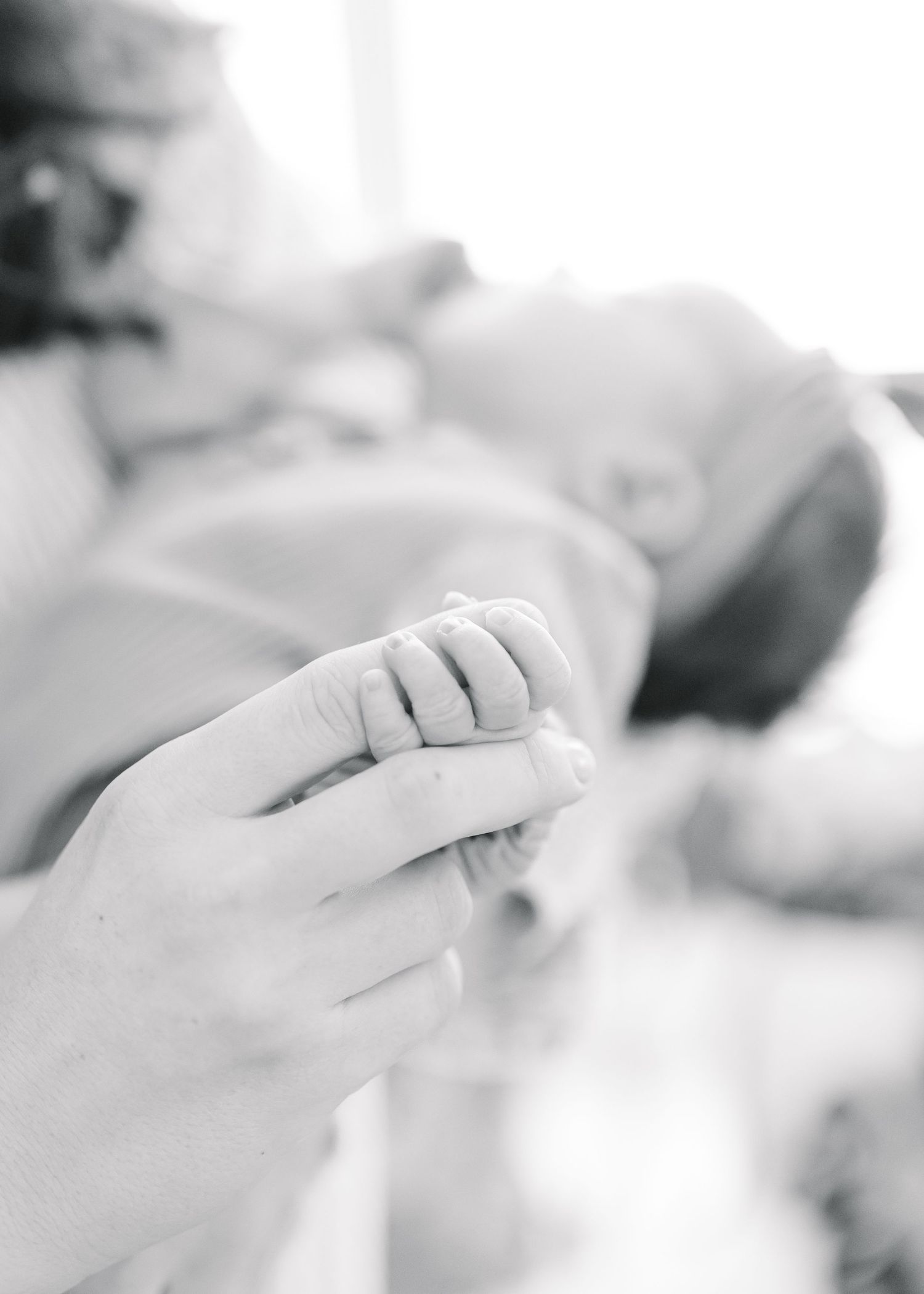 Close-up black and white photo of a newborn hand holding a mother's finger.