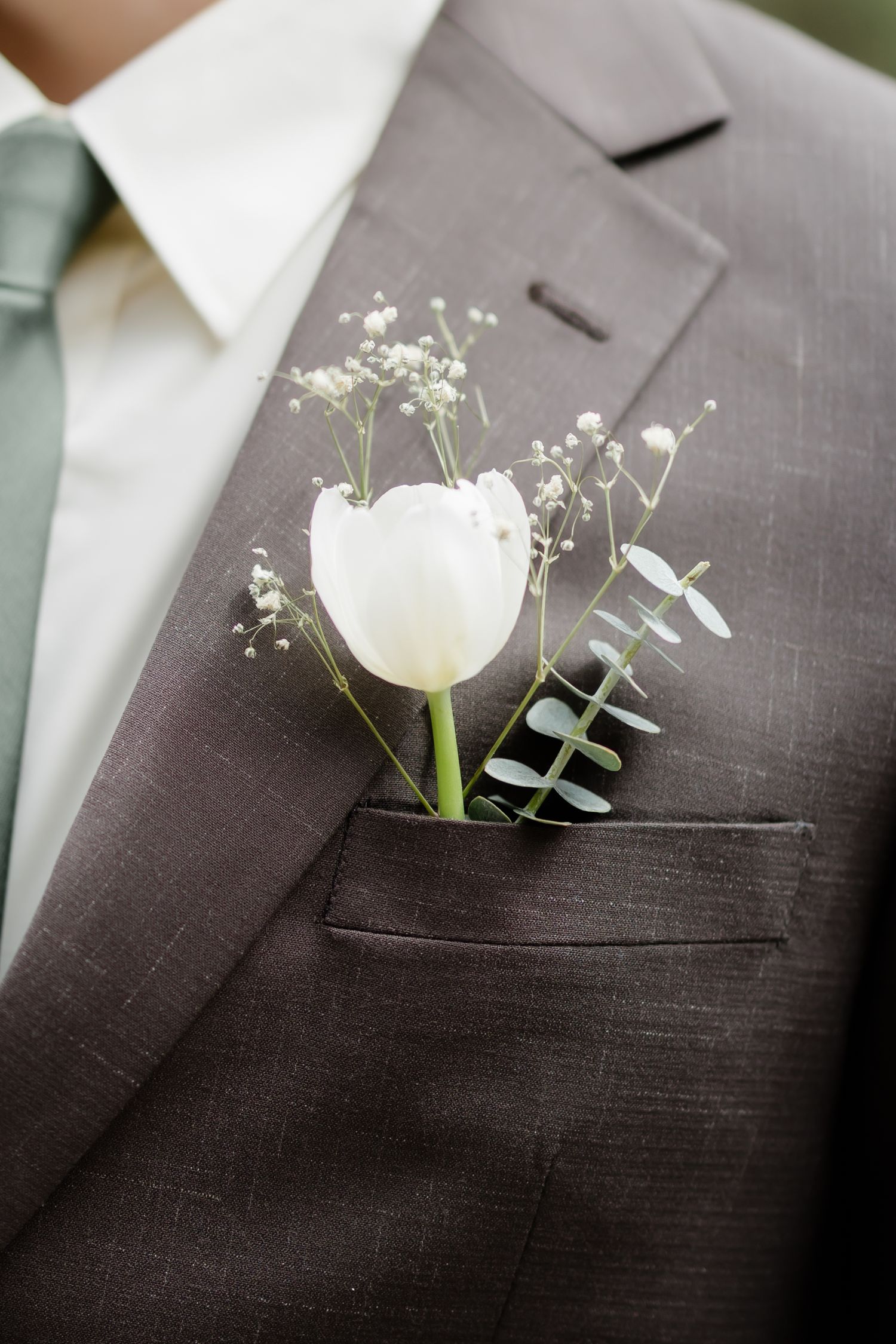 White tulip boutonniere with baby's breath and eucalyptus on a dark gray suit lapel pocket.