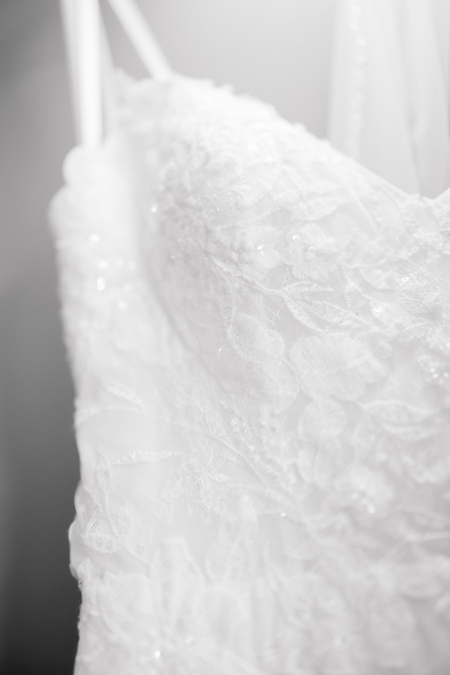 Close-up of an elegant white lace wedding dress with floral embroidery and delicate beading in black and white.