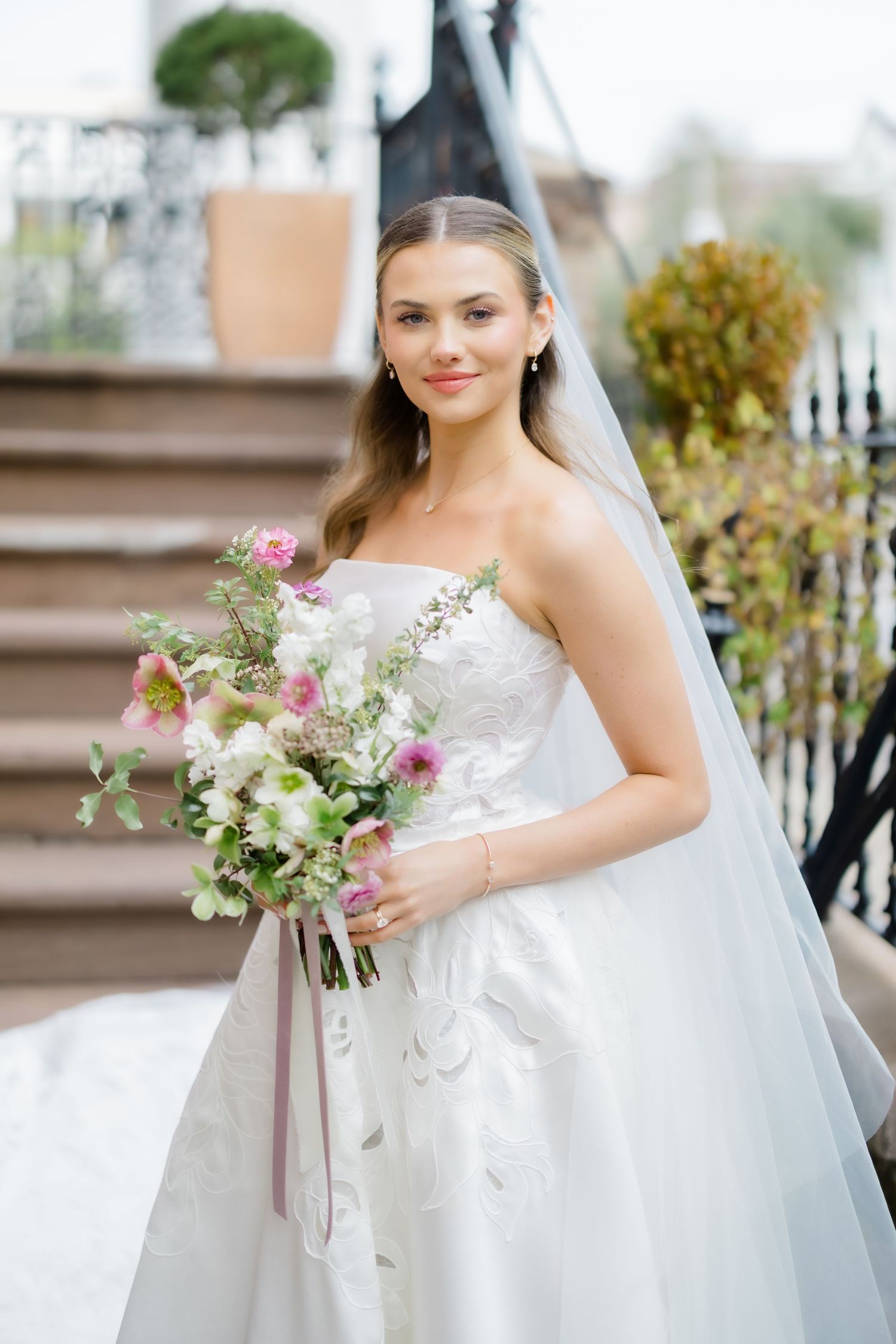 A bride in a classic white strapless wedding gown holds a romantic bouquet of pink and white flowers with flowing ribbons.