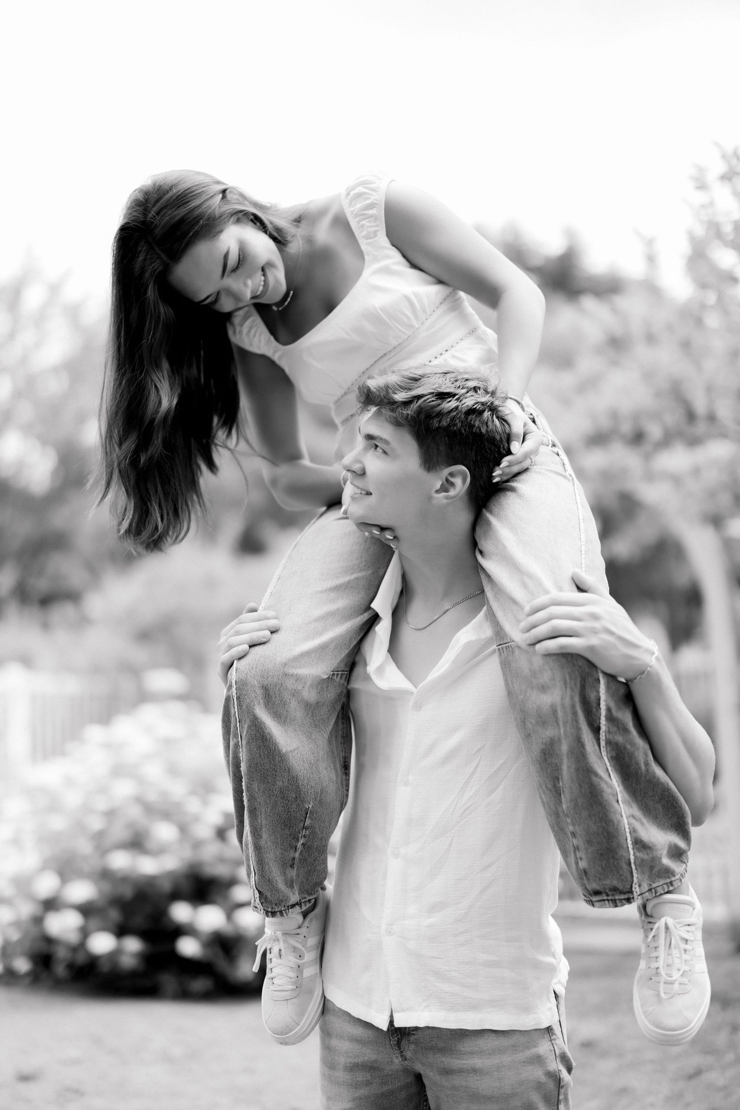 A smiling young man gives a laughing woman a piggyback ride outdoors in a black and white photo.