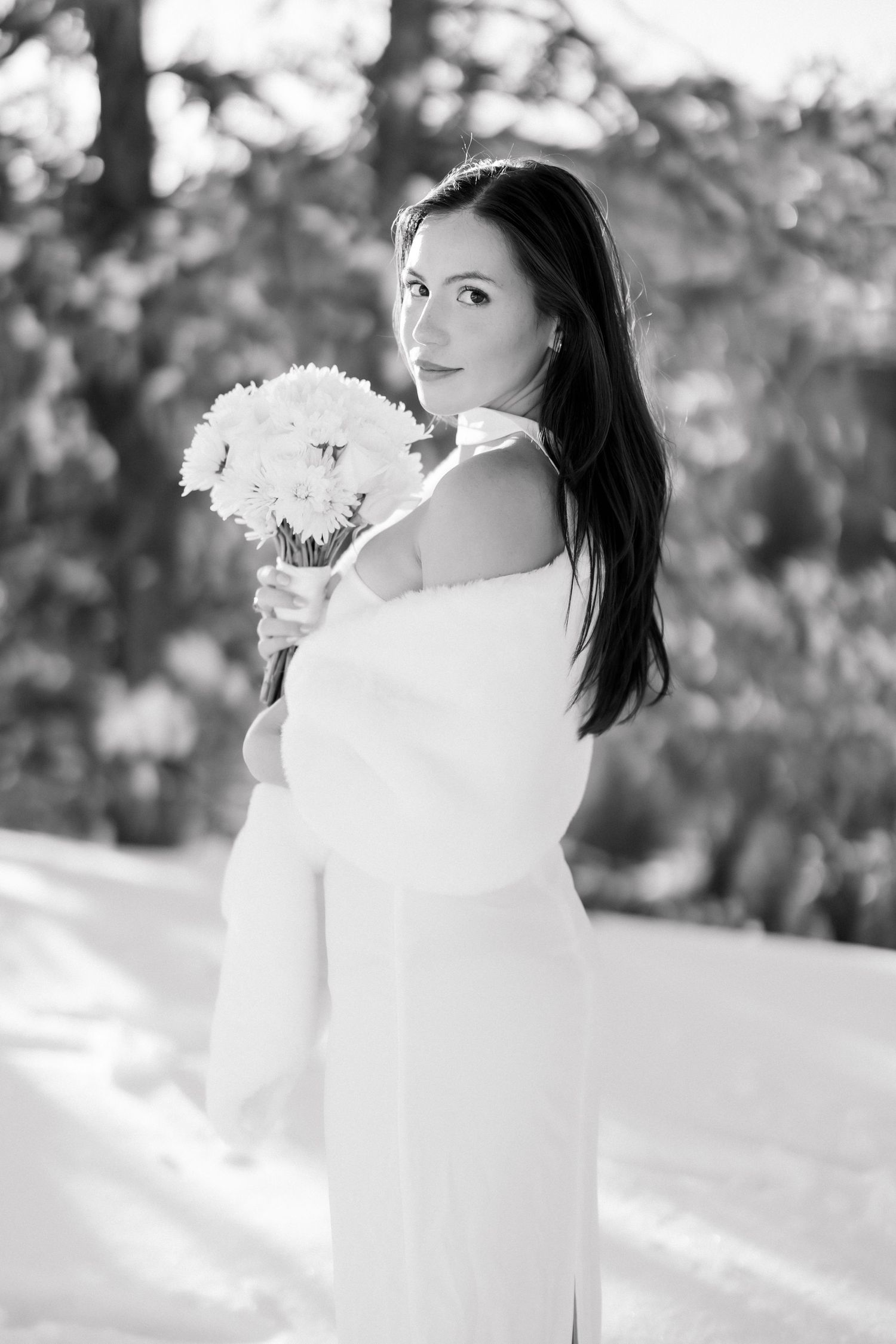 Black and white portrait of bride holding white flower bouquet in winter snow.