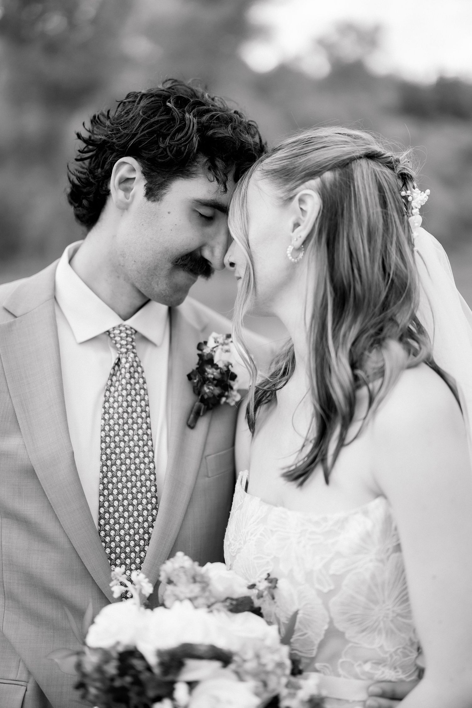 Black and white photo of a bride and groom touching foreheads tenderly on their wedding day.