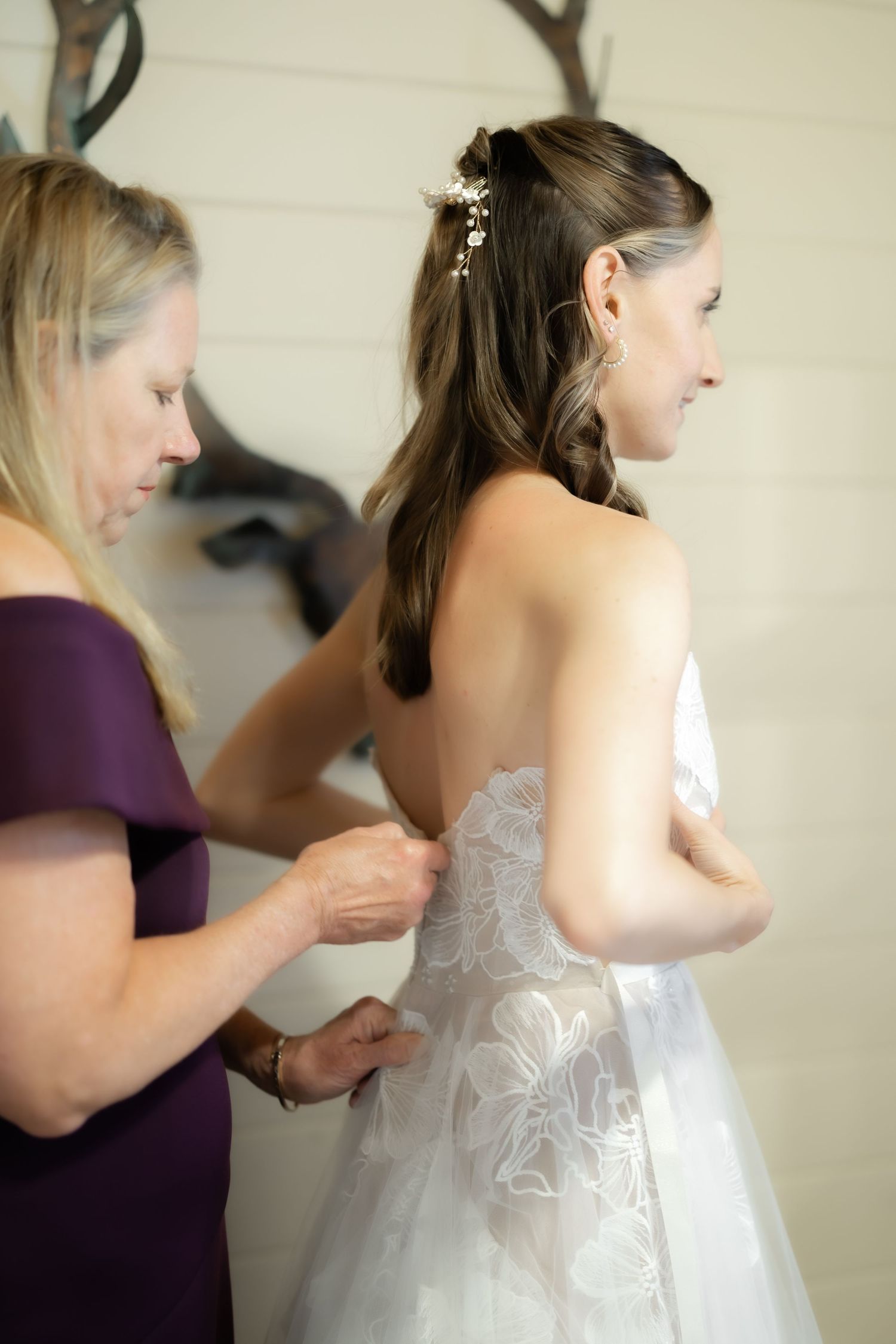 Woman in purple dress fastening the back of a bride's white lace wedding gown before the ceremony.