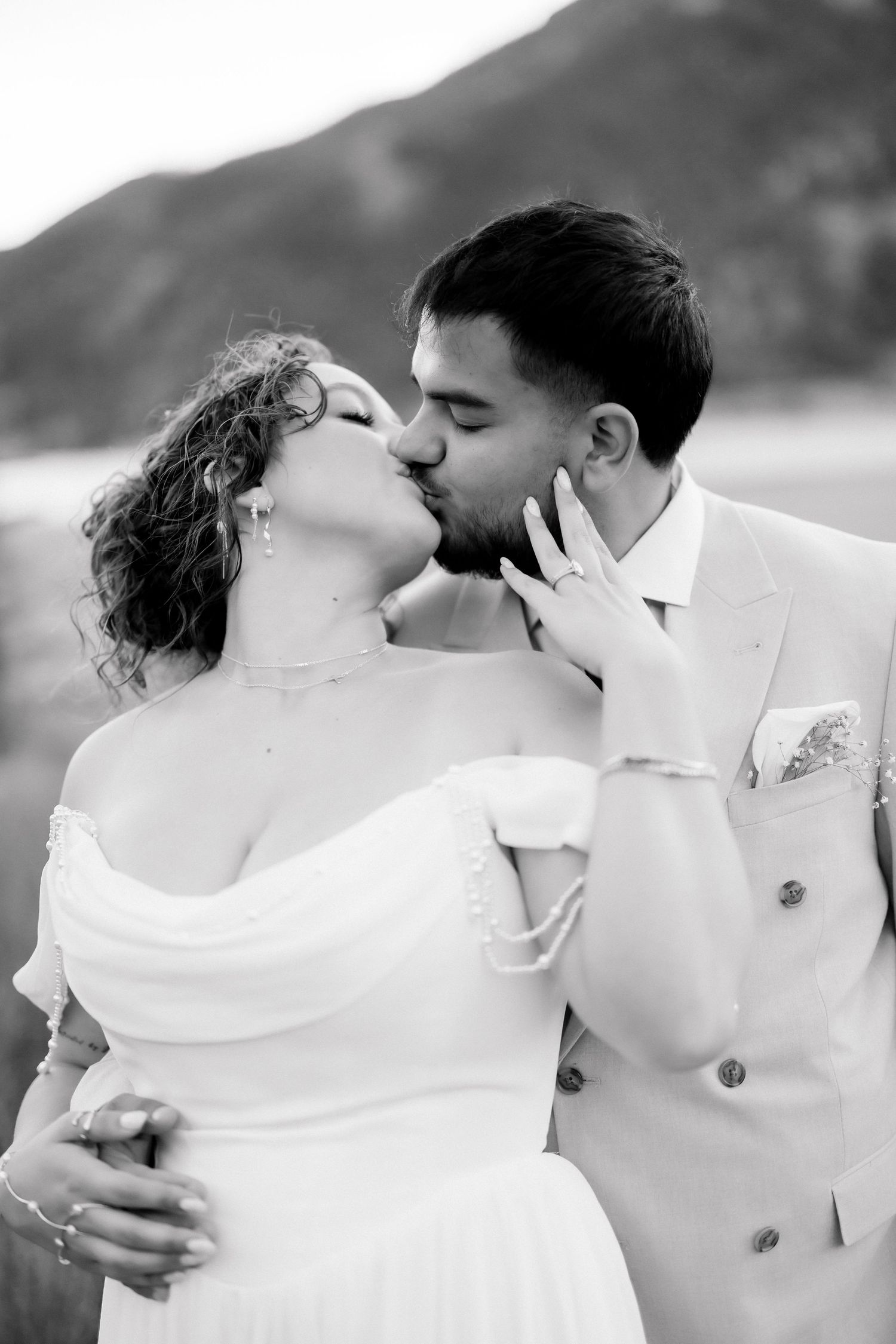 Black and white romantic kiss between bride and groom outdoors with mountain scenery in the background.