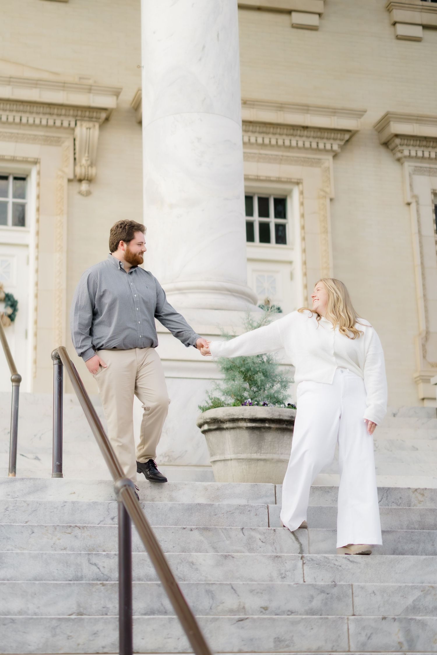 Couple holding hands on marble steps outside a grand building with large columns during an engagement photo session.