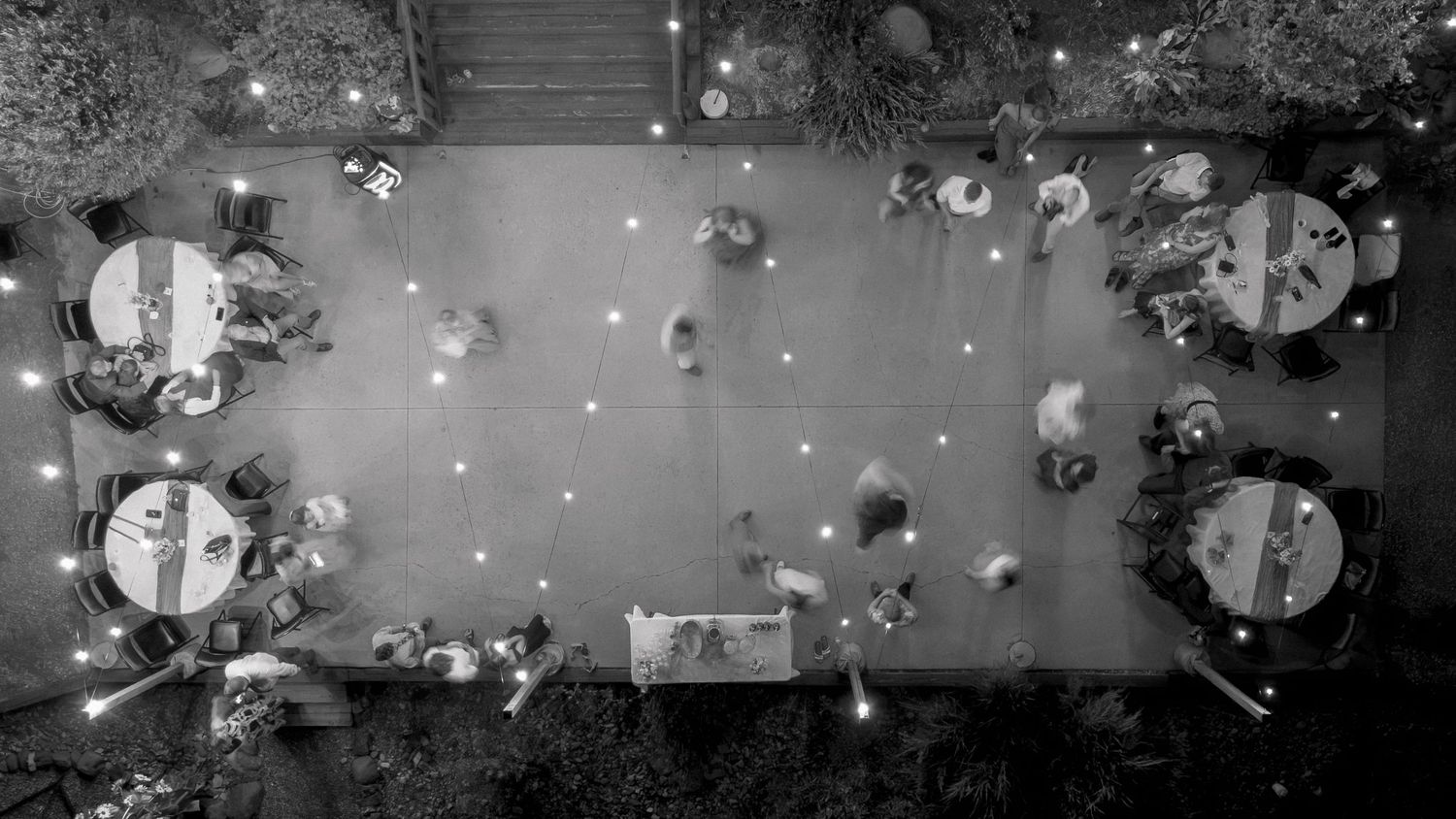 Aerial black and white photo of an elegant outdoor wedding reception with guests seated at round tables with candles.