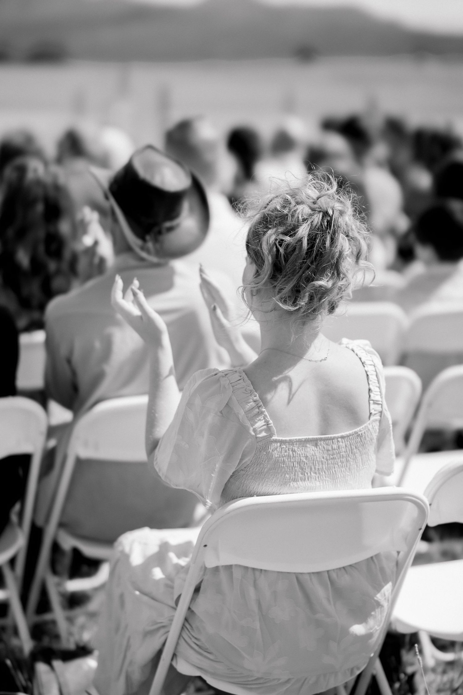 Black and white photo of wedding guests seated in white folding chairs at an outdoor ceremony.