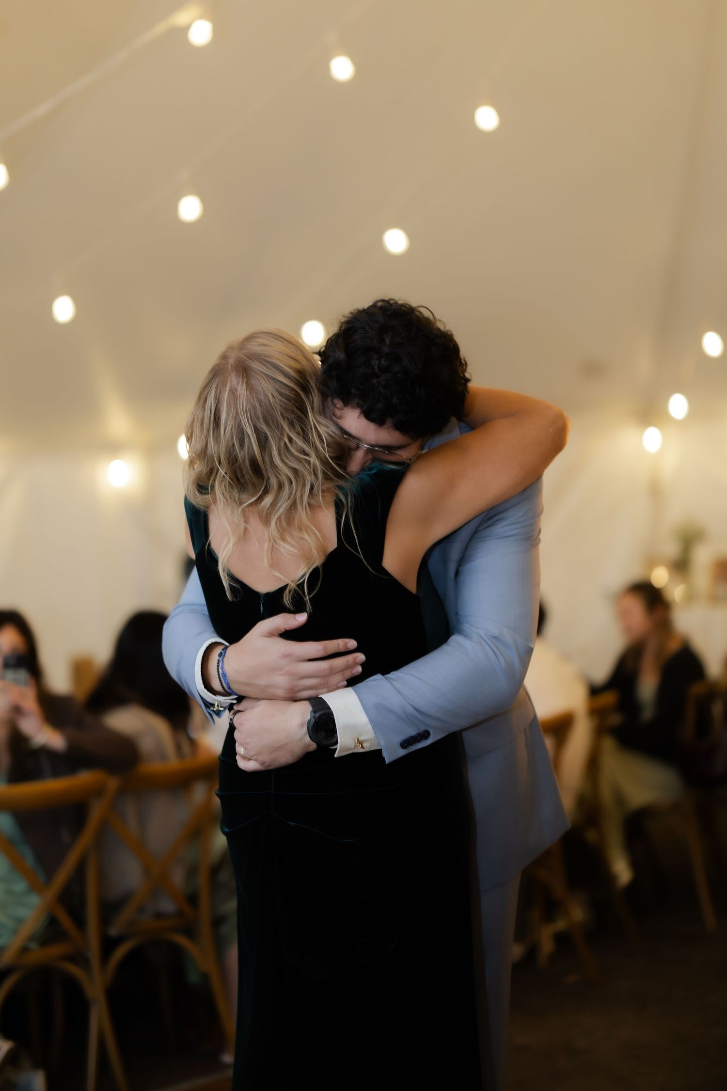 Groom sharing emotional dance embrace with mother at elegant tent wedding reception.