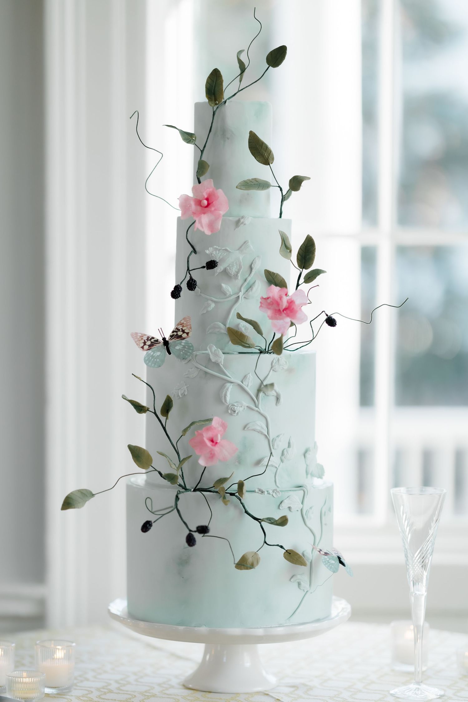 Pale blue wedding cake decorated with delicate pink flowers and greenery.