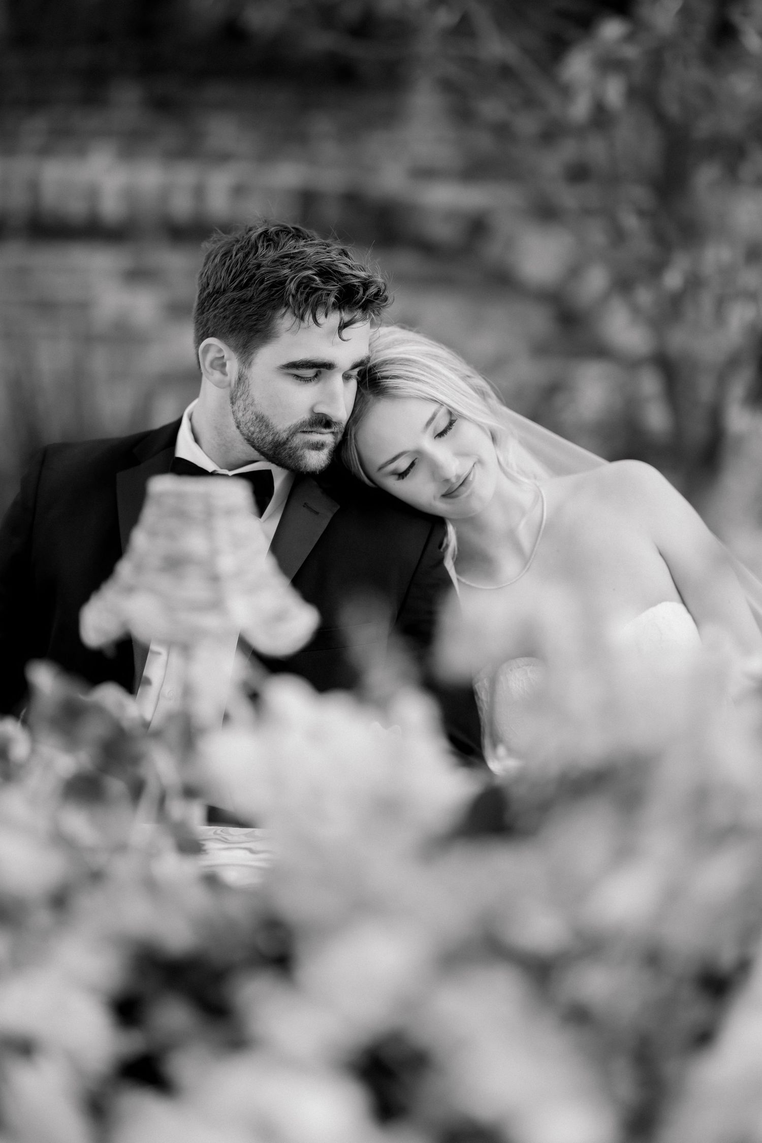 Black and white photo of a bride and groom sharing a tender moment at their wedding reception table.