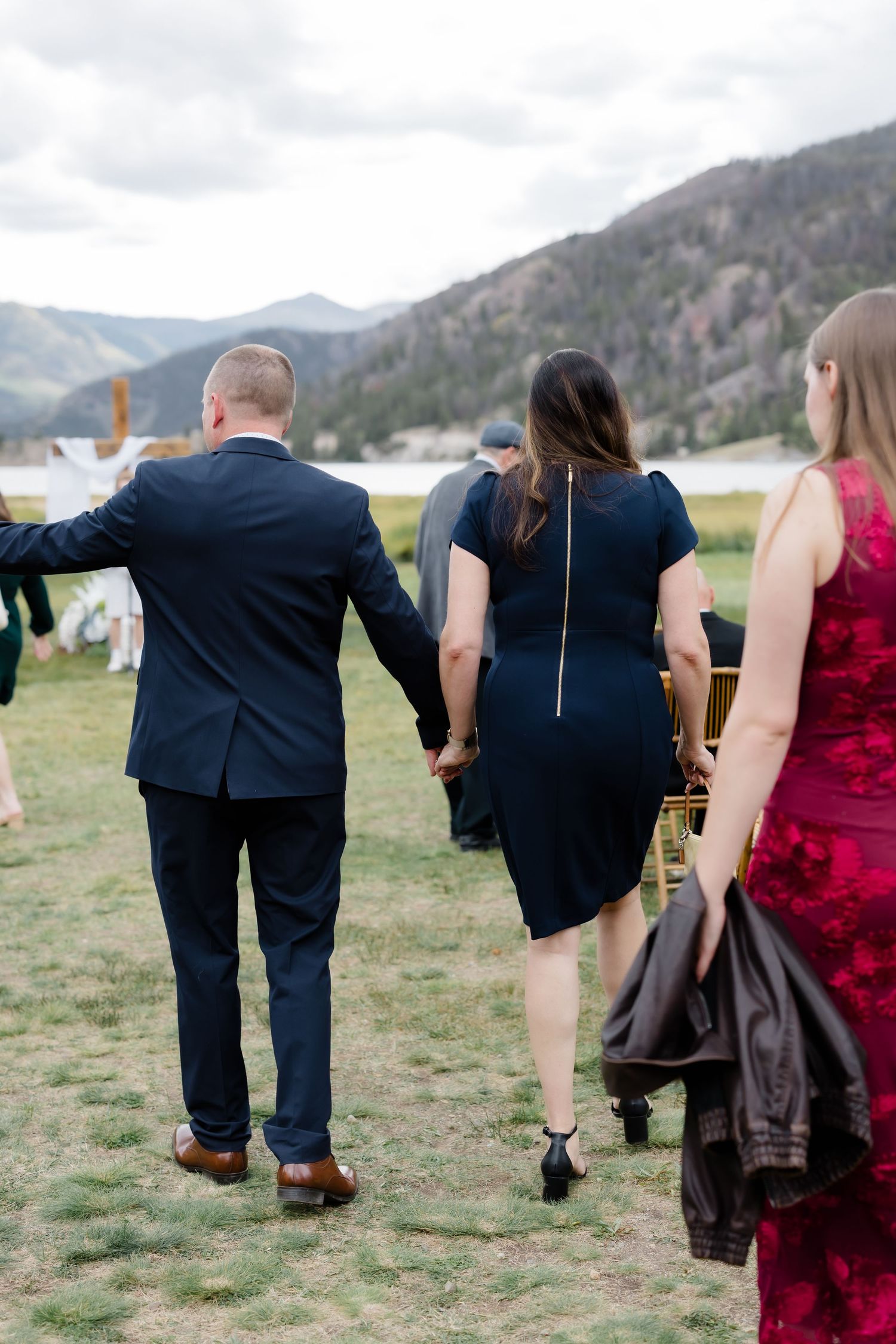 Wedding guests holding hands walking toward an outdoor mountain lakeside ceremony venue.