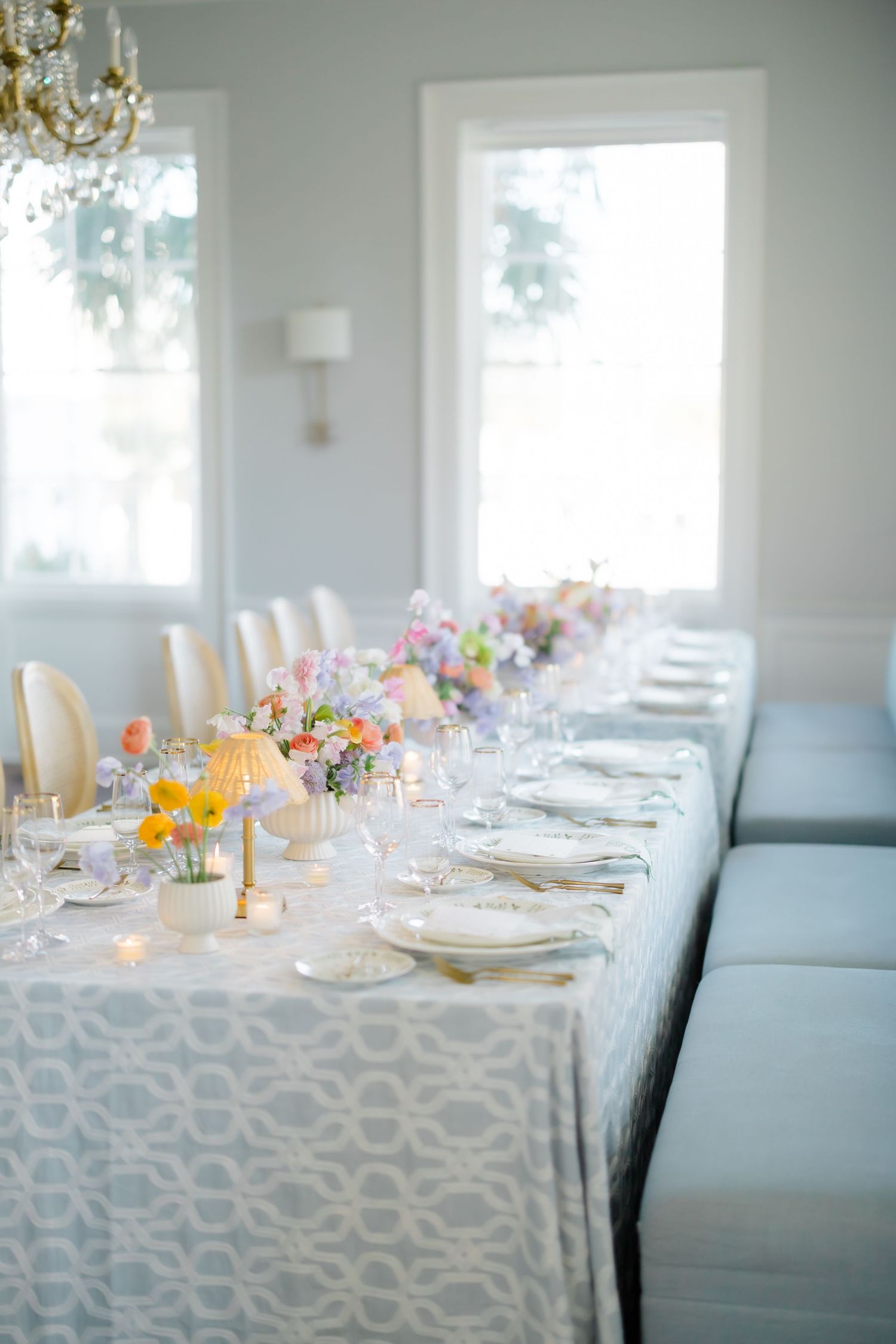 Elegant wedding reception table with pastel floral centerpieces, white geometric tablecloth, and gold accents in a bright dining room.