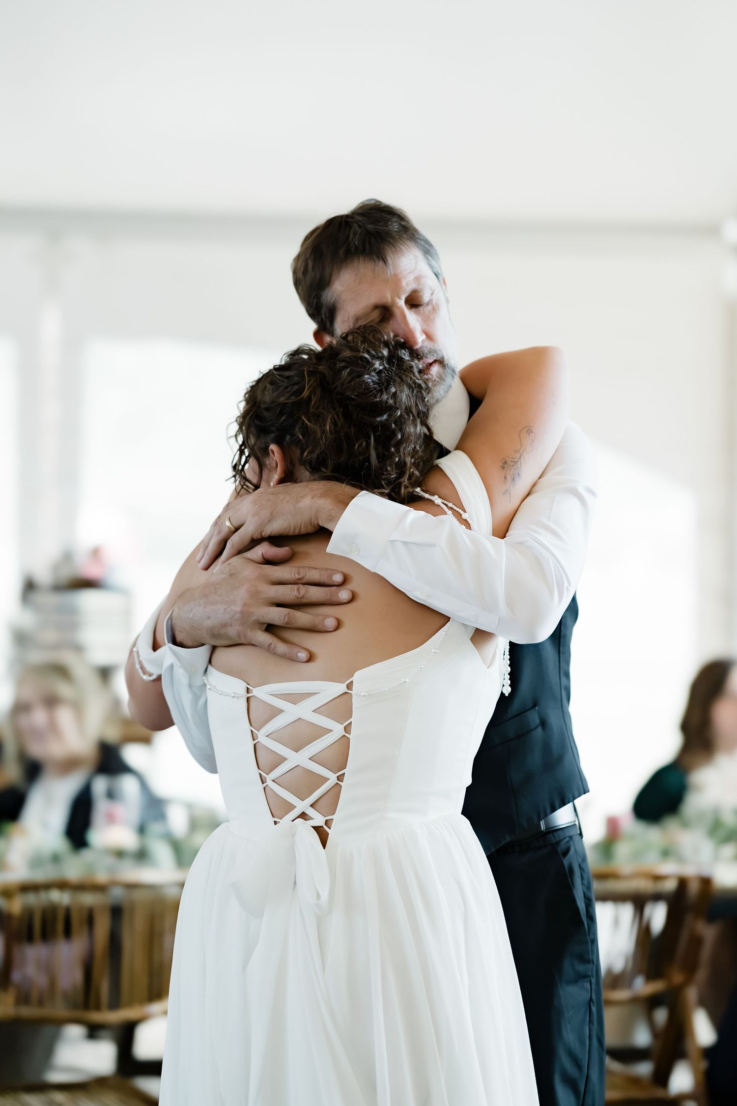 Emotional father-daughter dance as bride in lace-back gown embraces father at wedding reception.