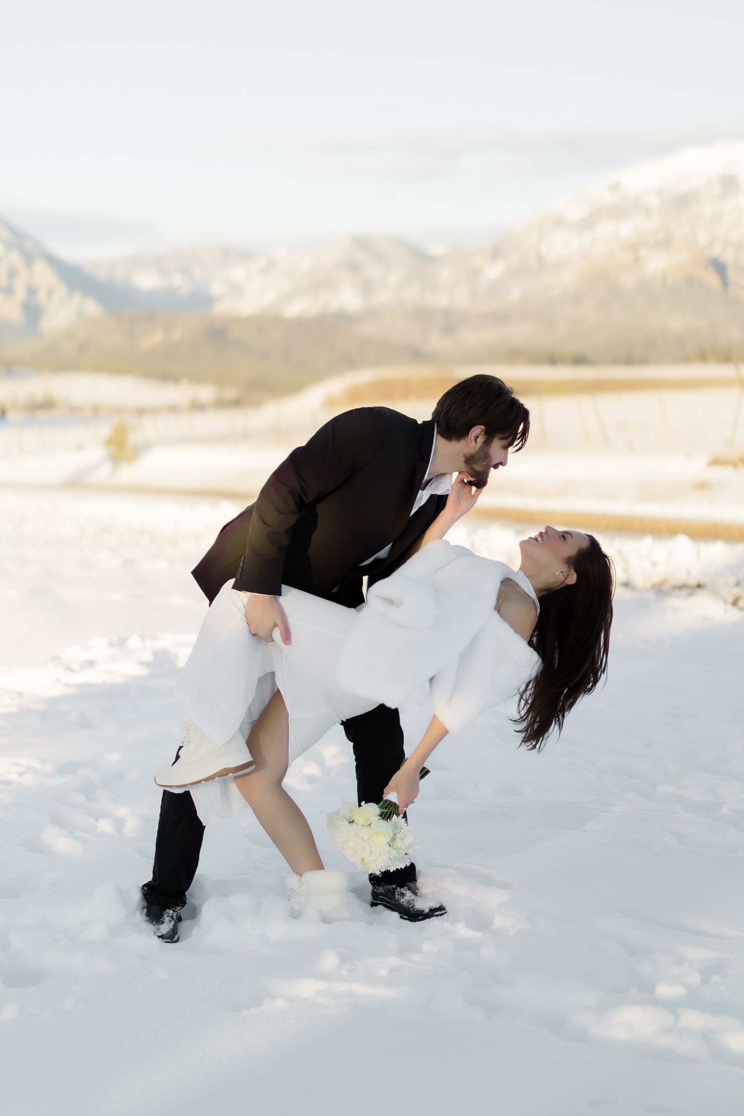 Groom dipping bride dramatically in the snow during a winter wedding outdoor photo session.