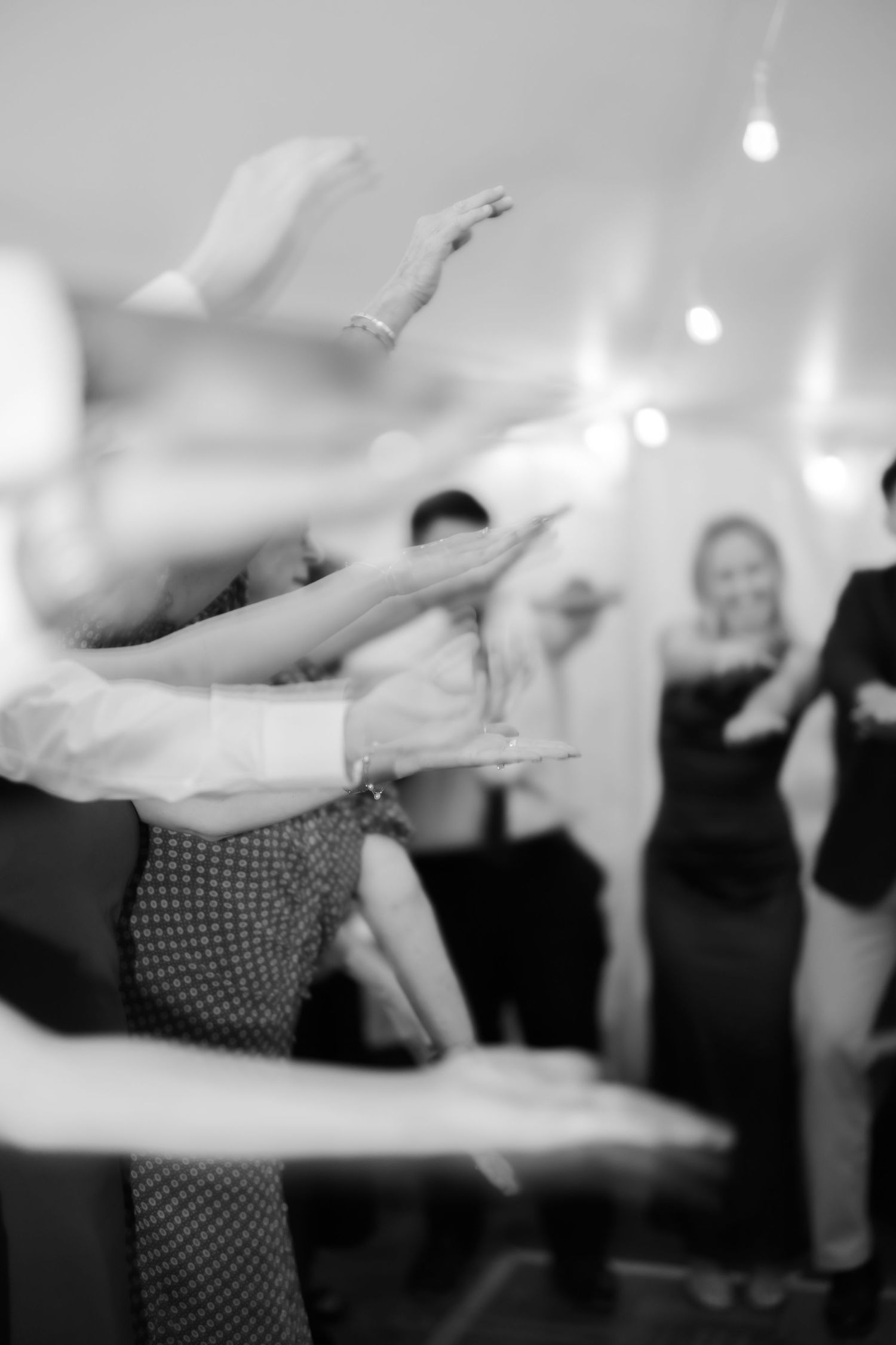 Black and white photo of people dancing with arms raised at an indoor event or party.