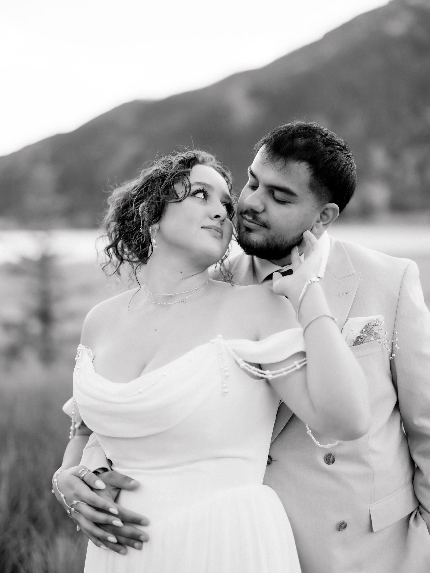 Black and white wedding photo of bride and groom embracing outdoors with mountain backdrop.