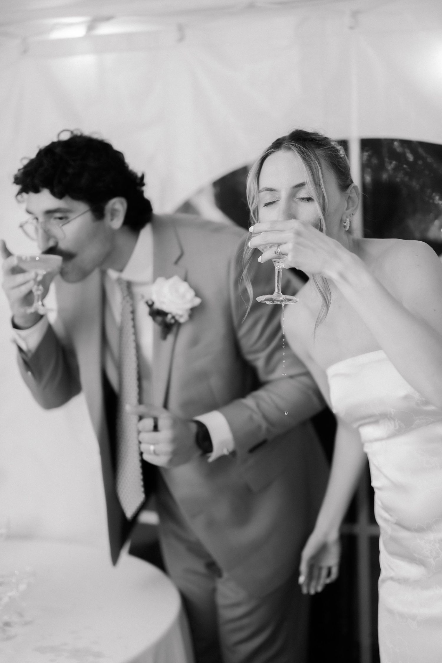 Black and white photo of bride and groom toasting with champagne glasses at their wedding reception.