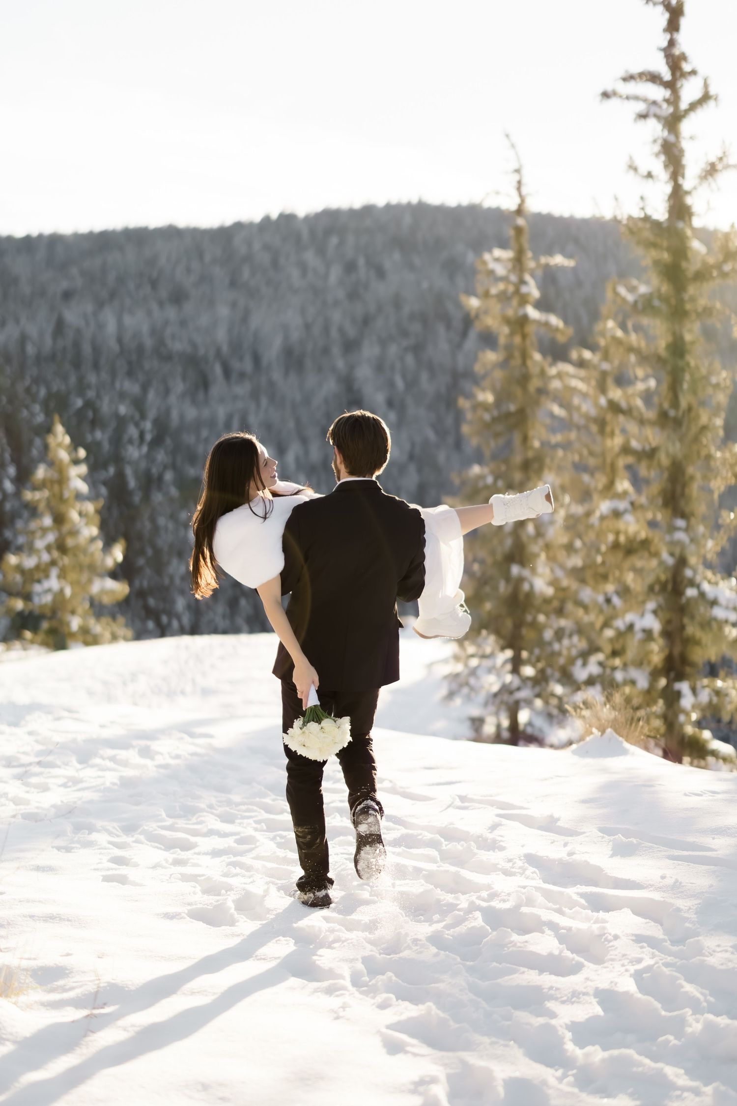 Bride and groom walk away through snowy mountain landscape, bride gesturing with outstretched arm.