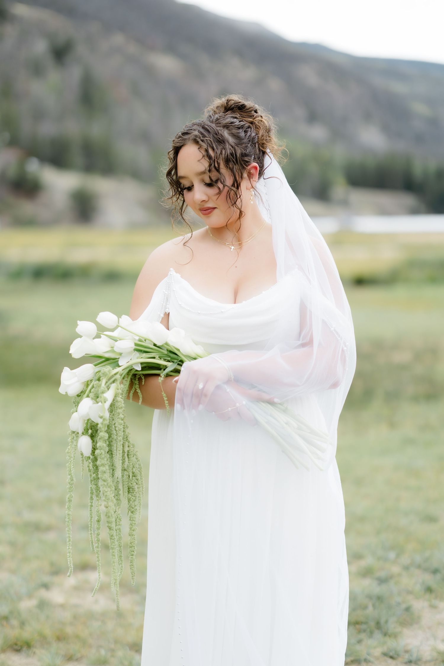 Bride in white gown holds tulip bouquet outdoors with mountain backdrop.