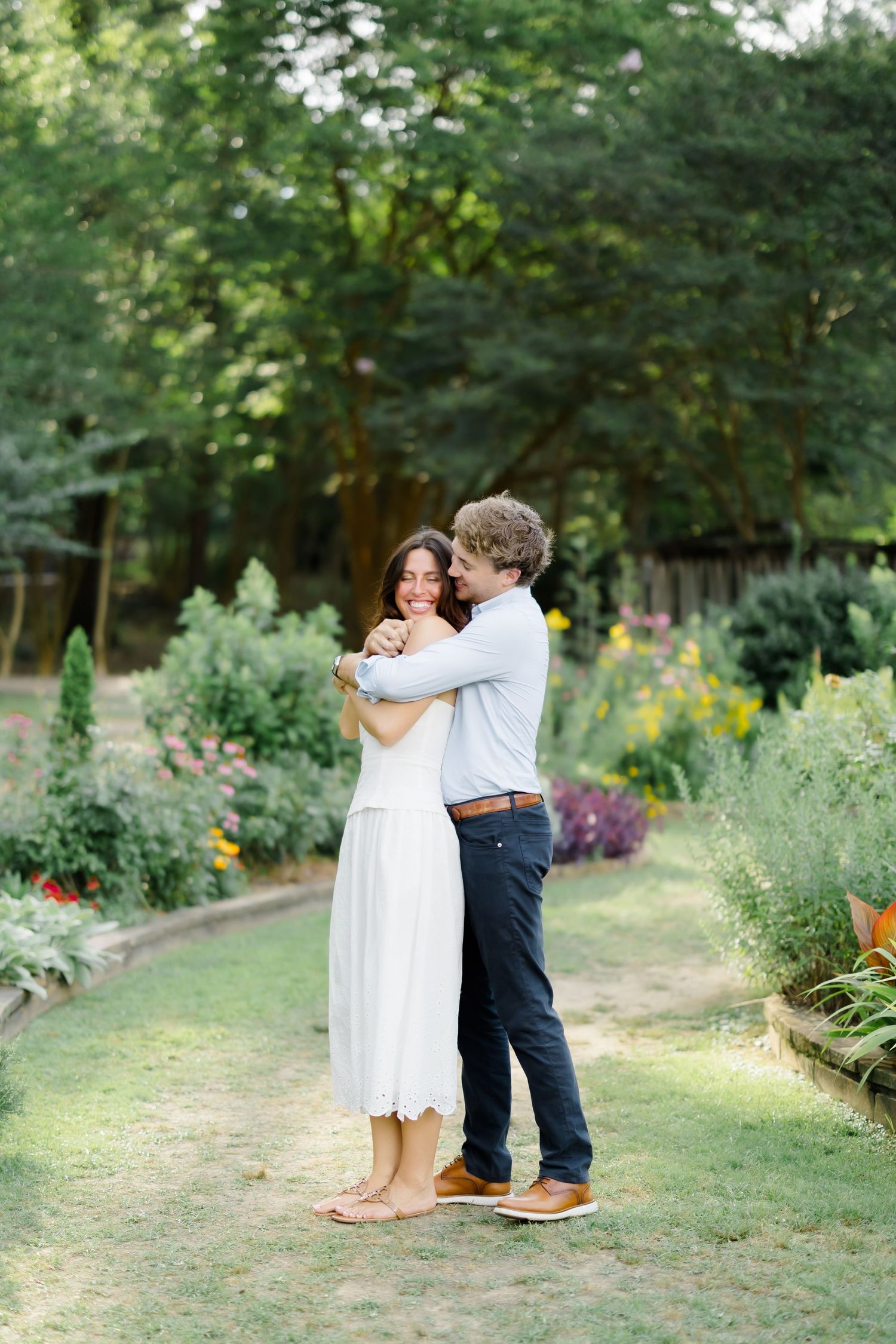 Happy couple hugging and smiling together along a beautiful garden path during an engagement shoot.