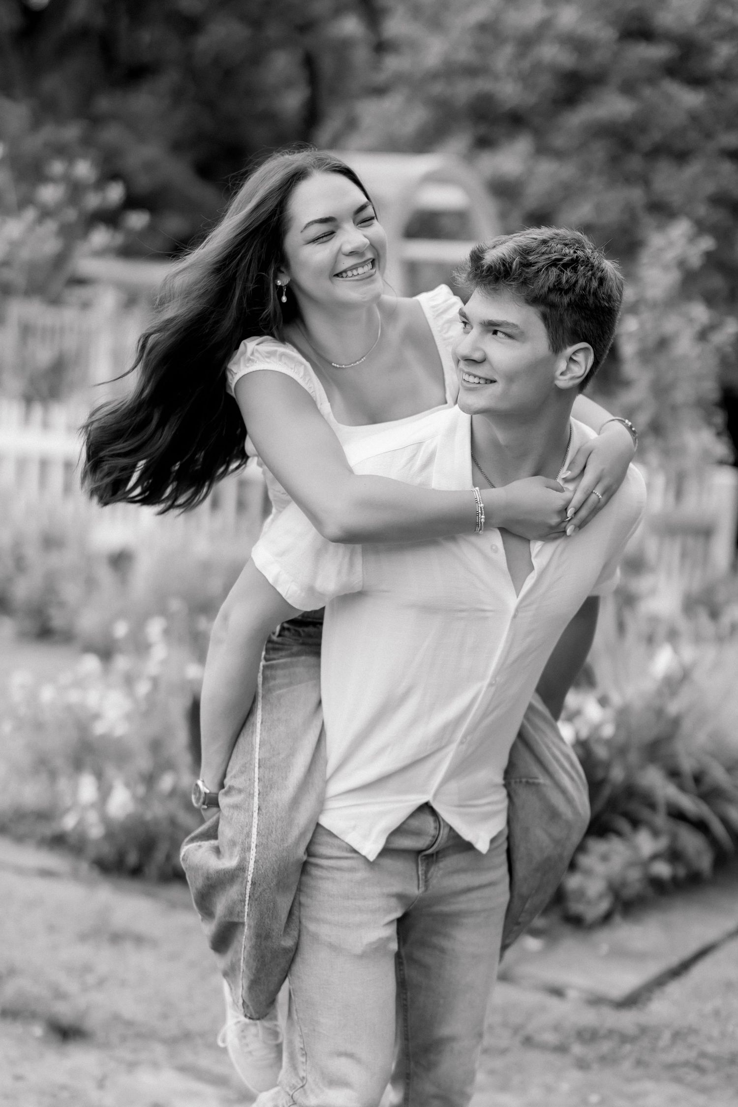 A joyful couple in black and white photo as young man gives woman a piggyback ride in a garden.