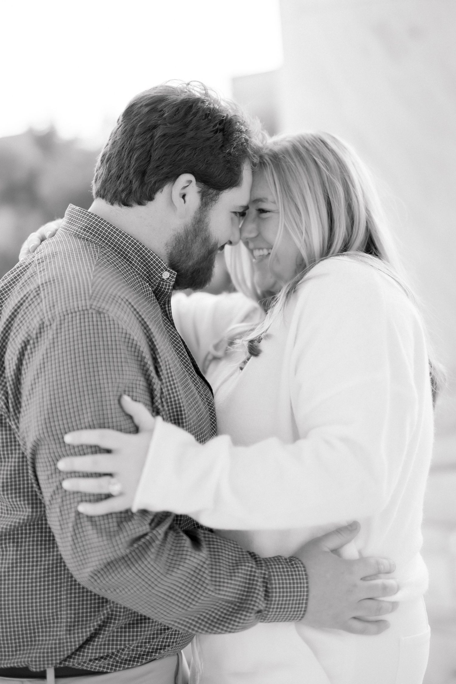Black and white photo of a couple embracing and smiling at each other during an engagement session.