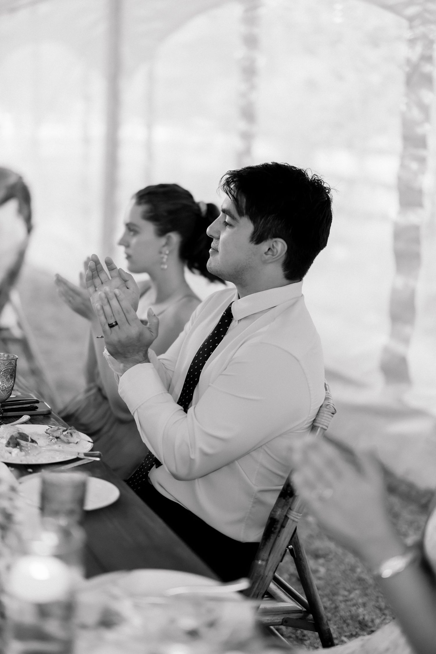 Black and white photo of wedding guests applauding during speeches at elegant reception.