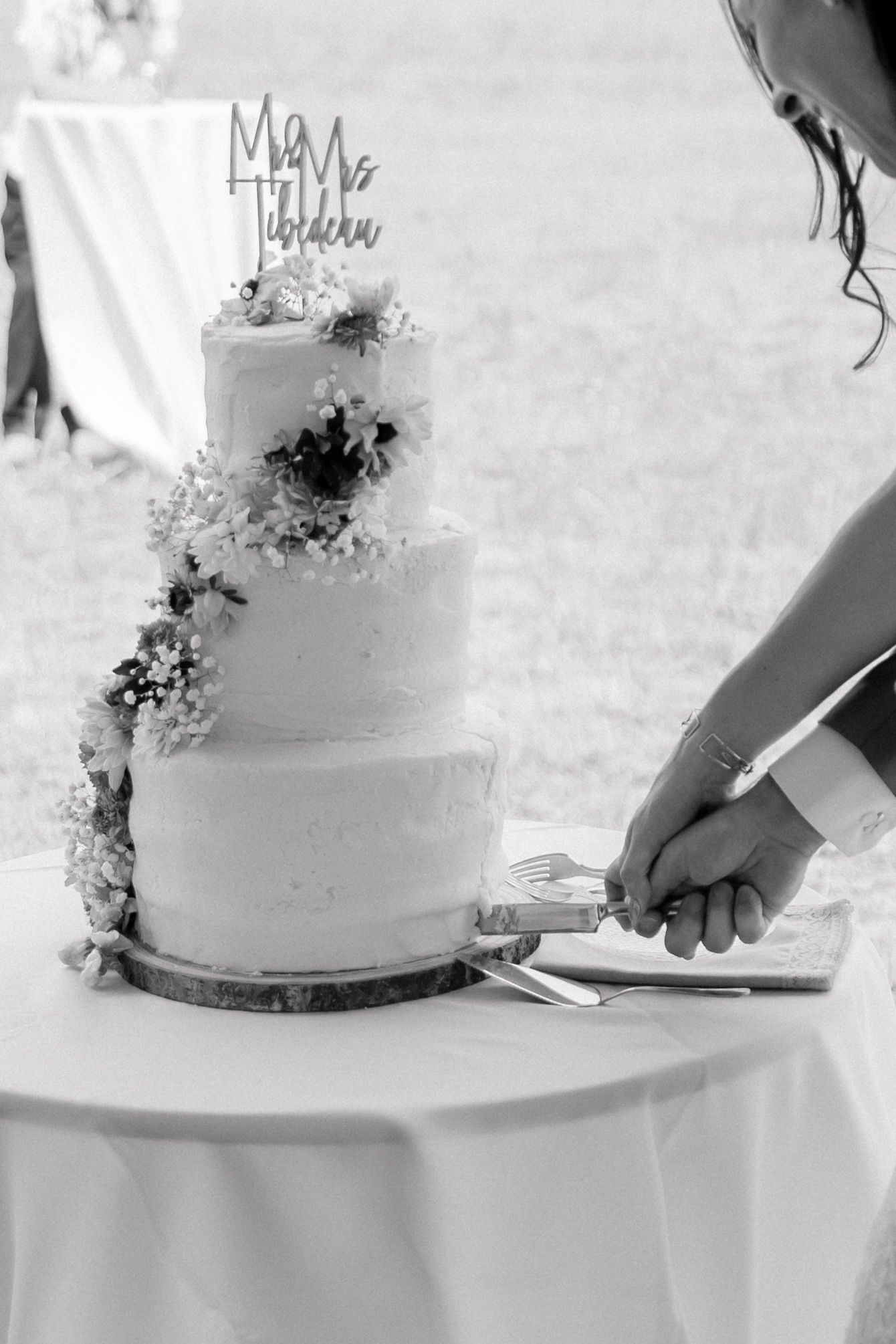 Black and white photo of a couple cutting a three-tier floral wedding cake topped with Mr & Mrs cake topper.