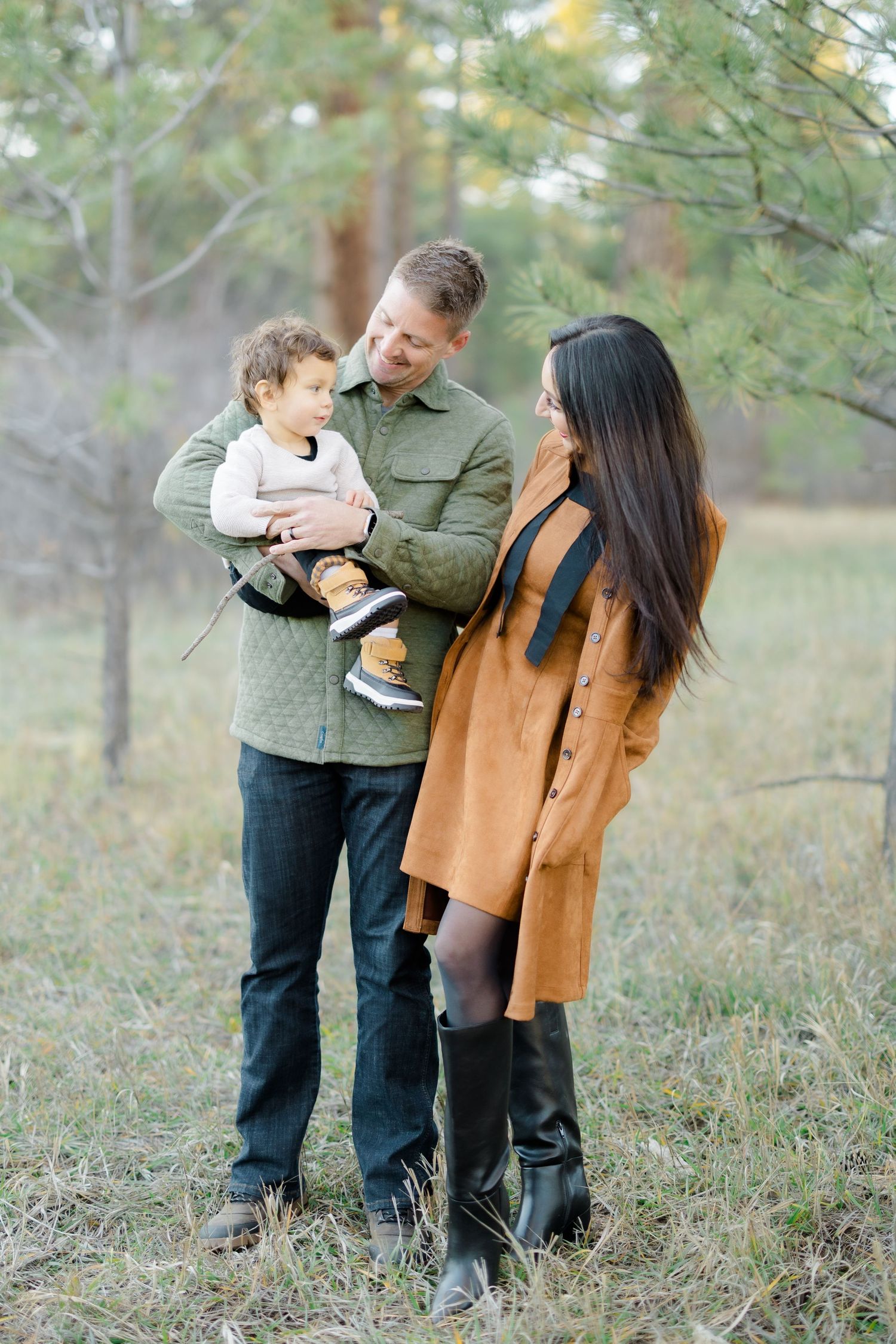 A couple and child play together outdoors in an autumn field wearing casual clothing.
